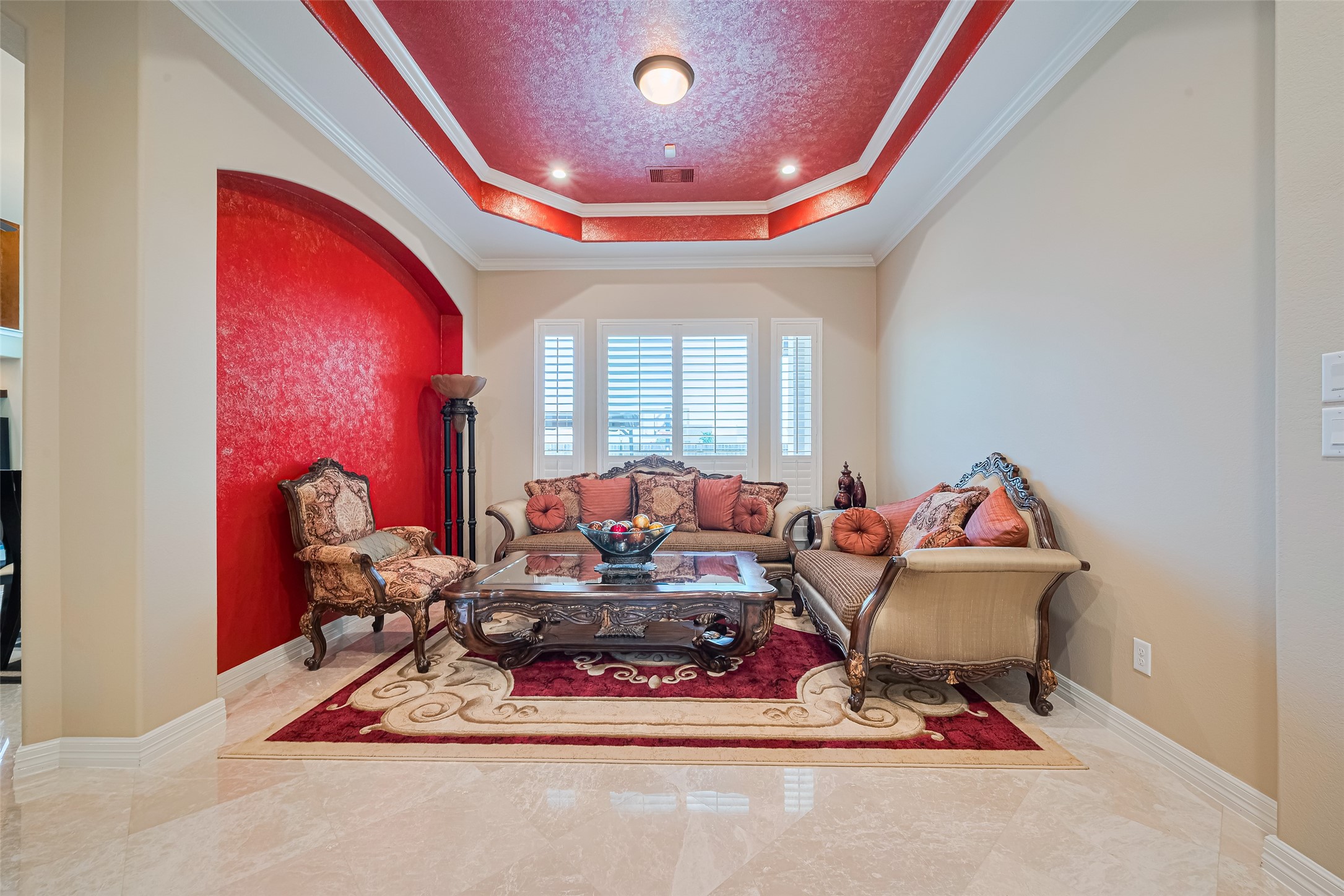 Inviting sitting room distinguished by a bold accent alcove, detailed ceiling treatment, and plantation-shuttered windows.