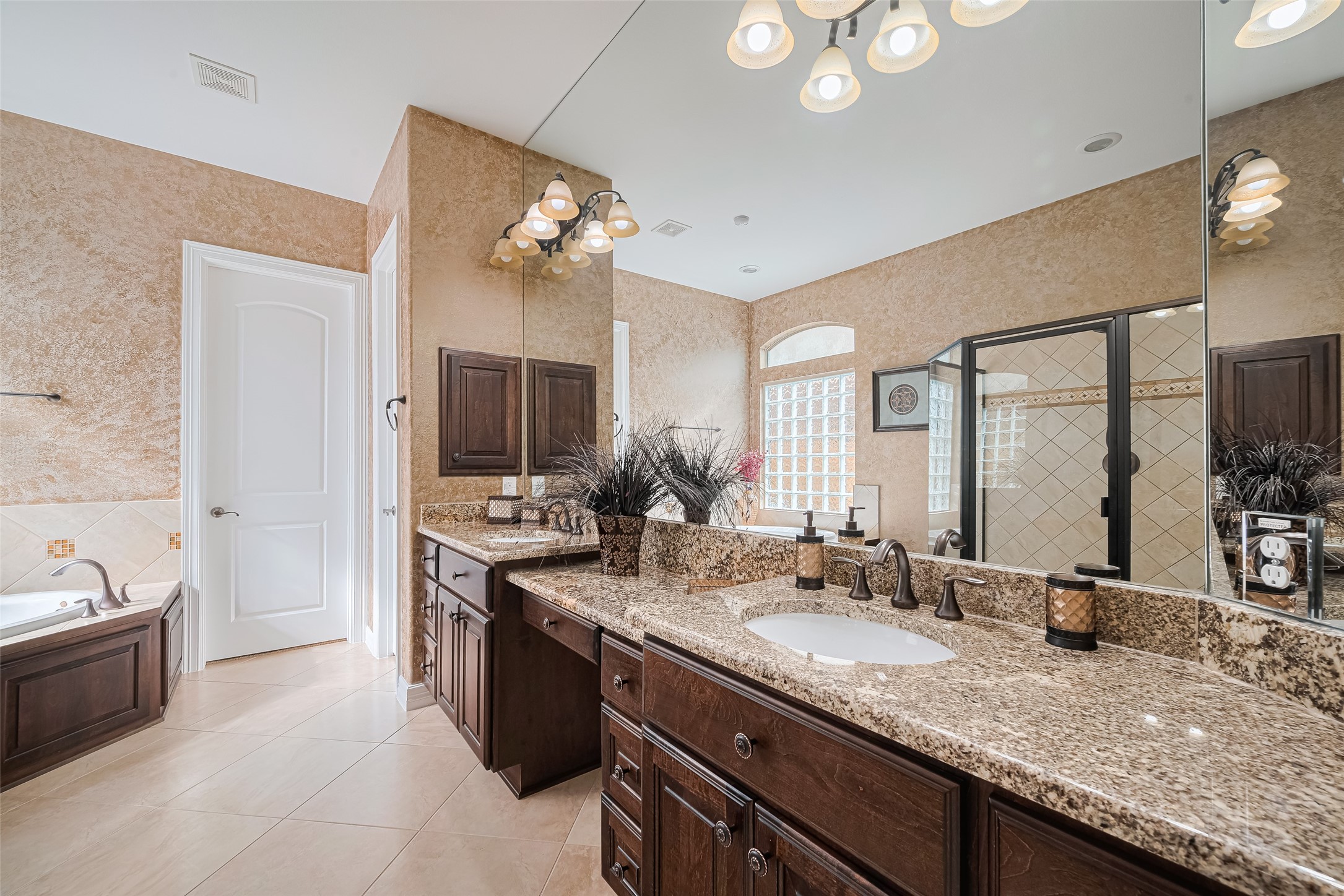 Spacious primary bathroom featuring an extended granite vanity, abundant cabinetry, oversized mirrors, and a separate walk-in shower.