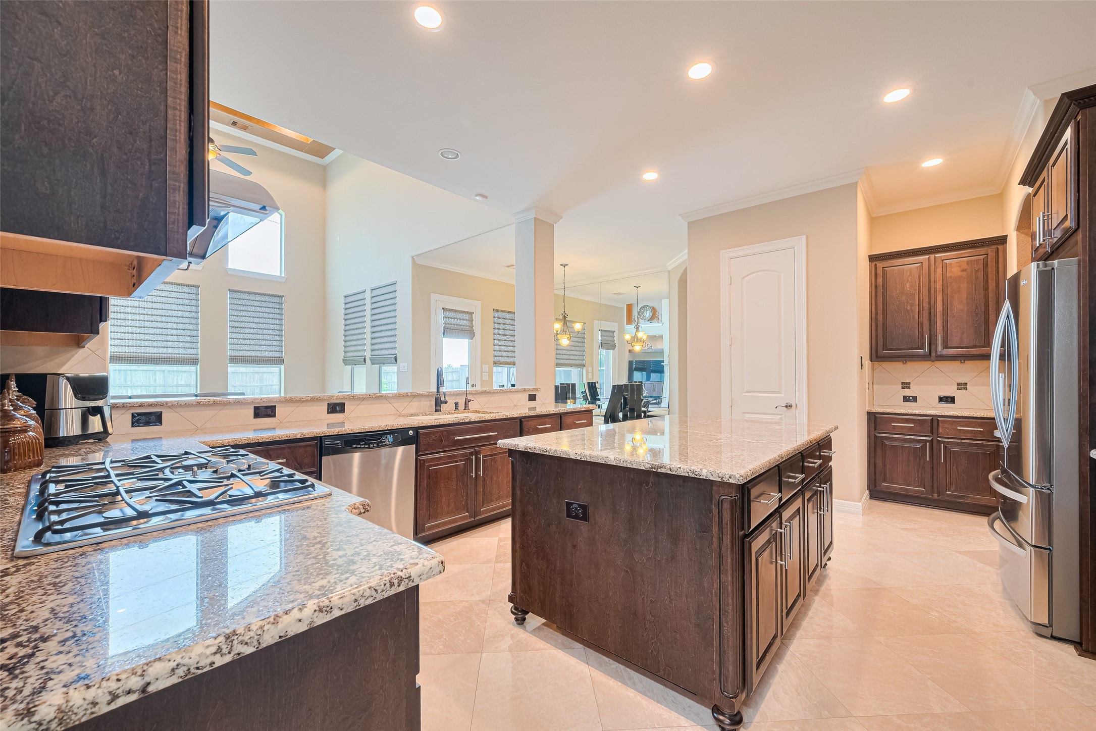 Wide kitchen view presenting the central island, generous workspace, rich wood finishes, and effortless flow into the adjoining living spaces.