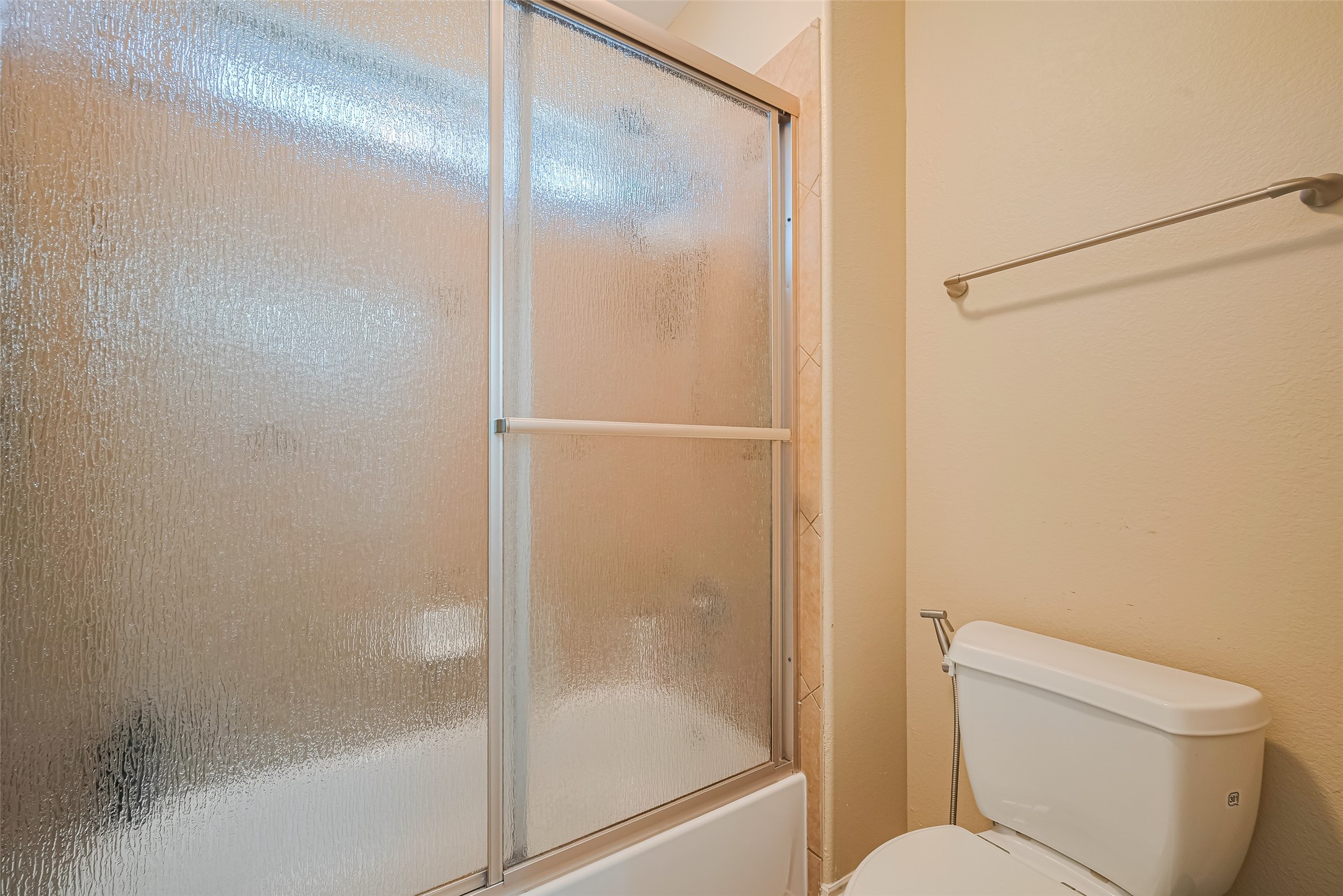 Secondary bathroom featuring a tub and shower combination with textured glass enclosure and neutral tile surround.