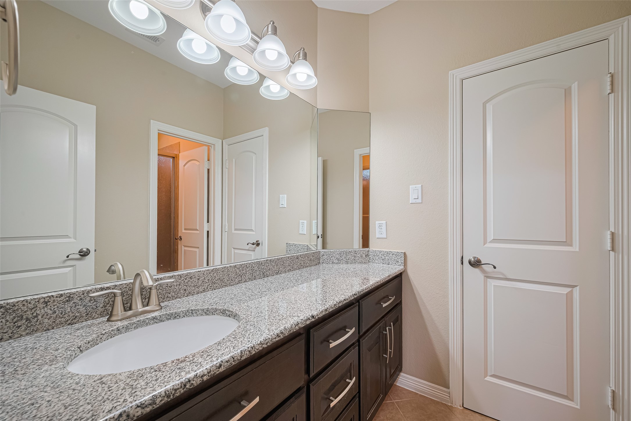 Well-appointed secondary bathroom featuring a spacious granite vanity, dark cabinetry, expansive mirror, and bright vanity lighting.