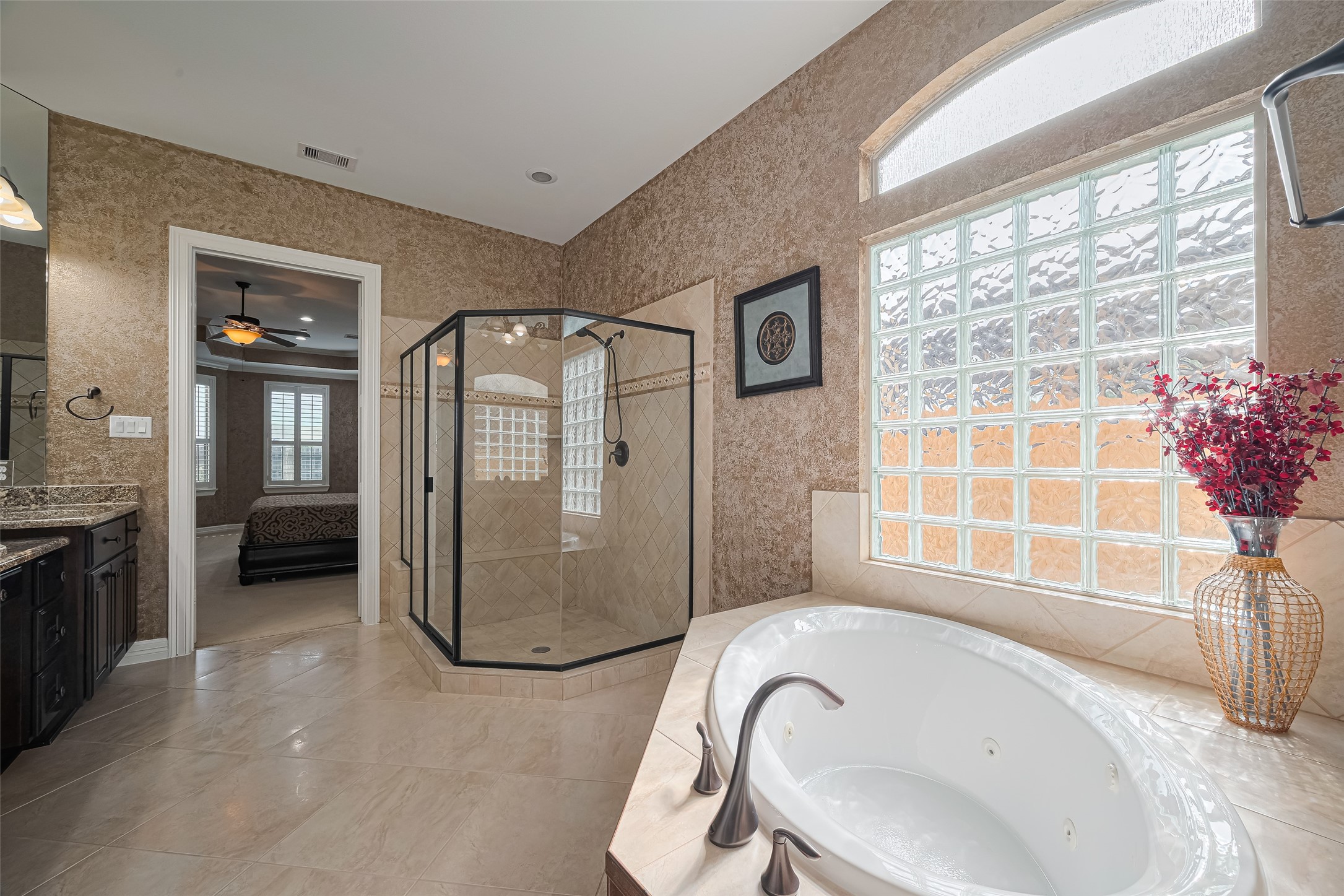 Spa-inspired primary bathroom featuring a jetted soaking tub, glass-enclosed walk-in shower, and beautiful natural light through glass-block windows.