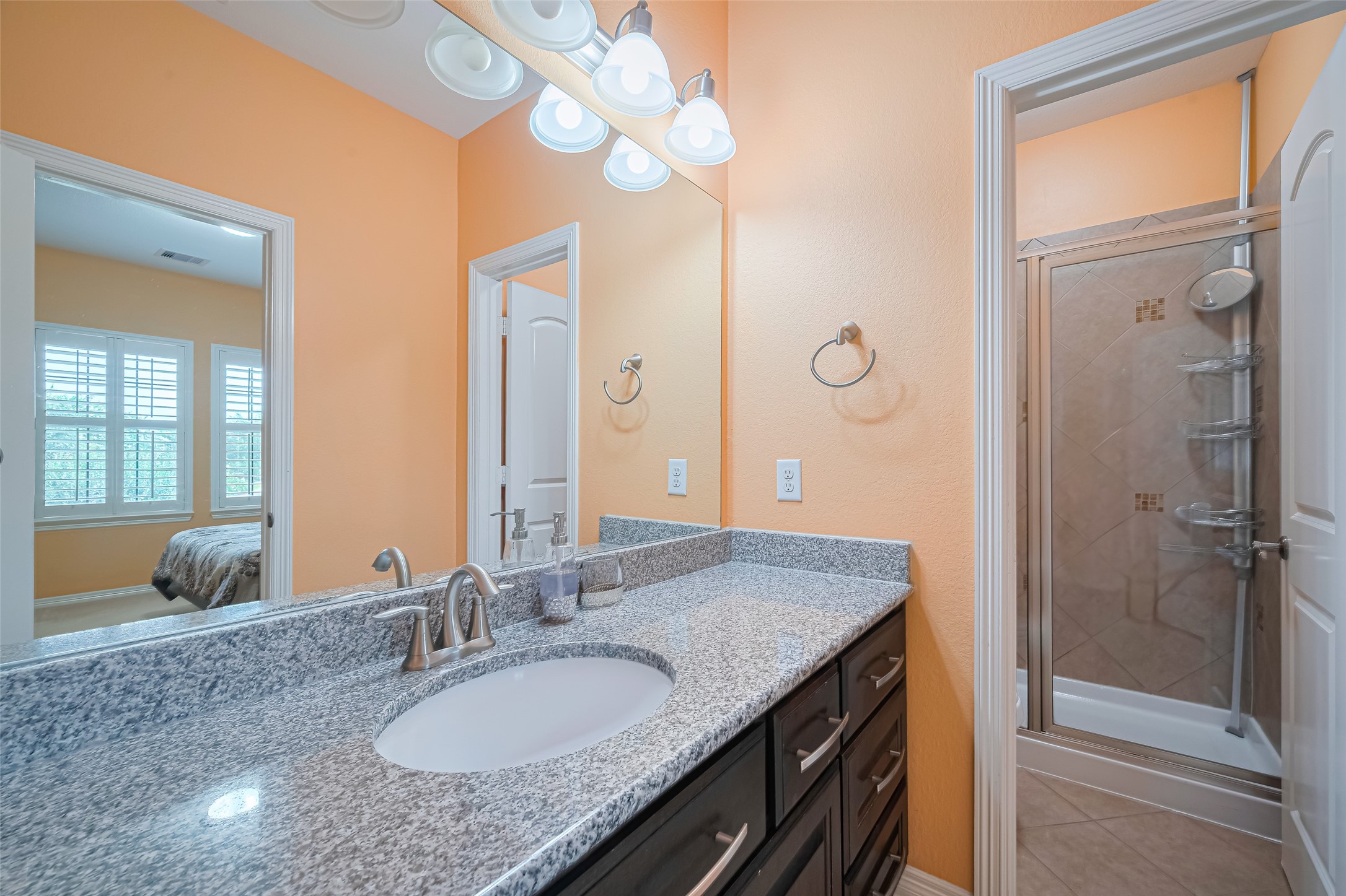 Fourth bathroom featuring a granite vanity, dark cabinetry, large mirror, and a separate tiled shower with glass enclosure.