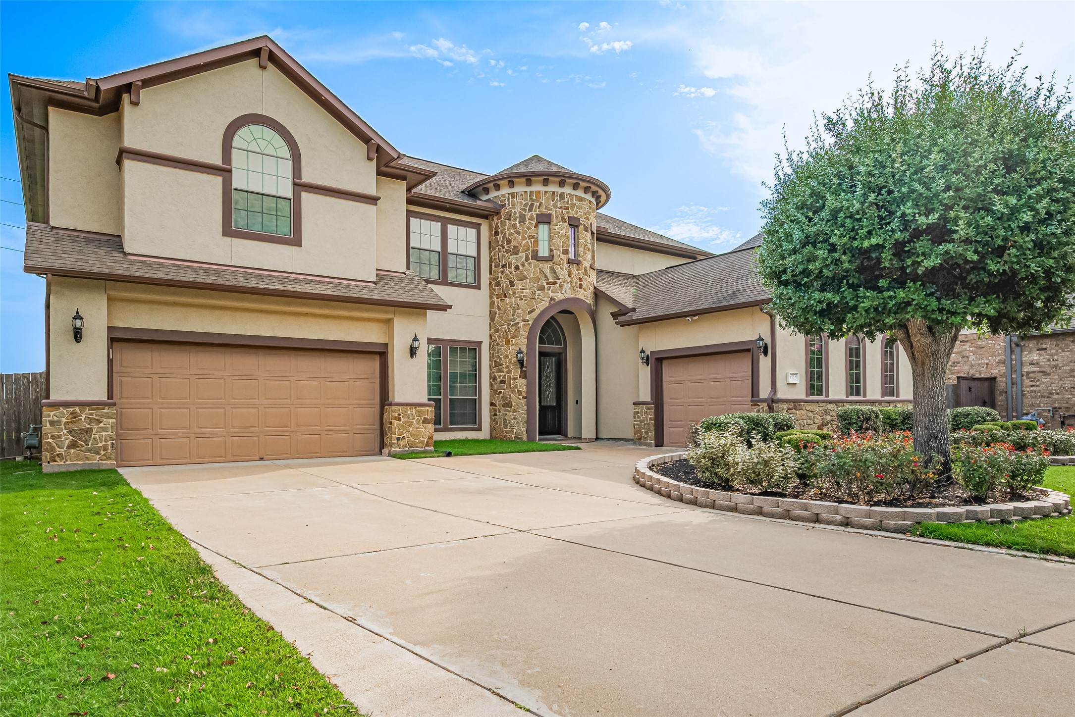 Grand driveway view highlighting the three-car garage, dramatic stone turret, and stately arched entryway.