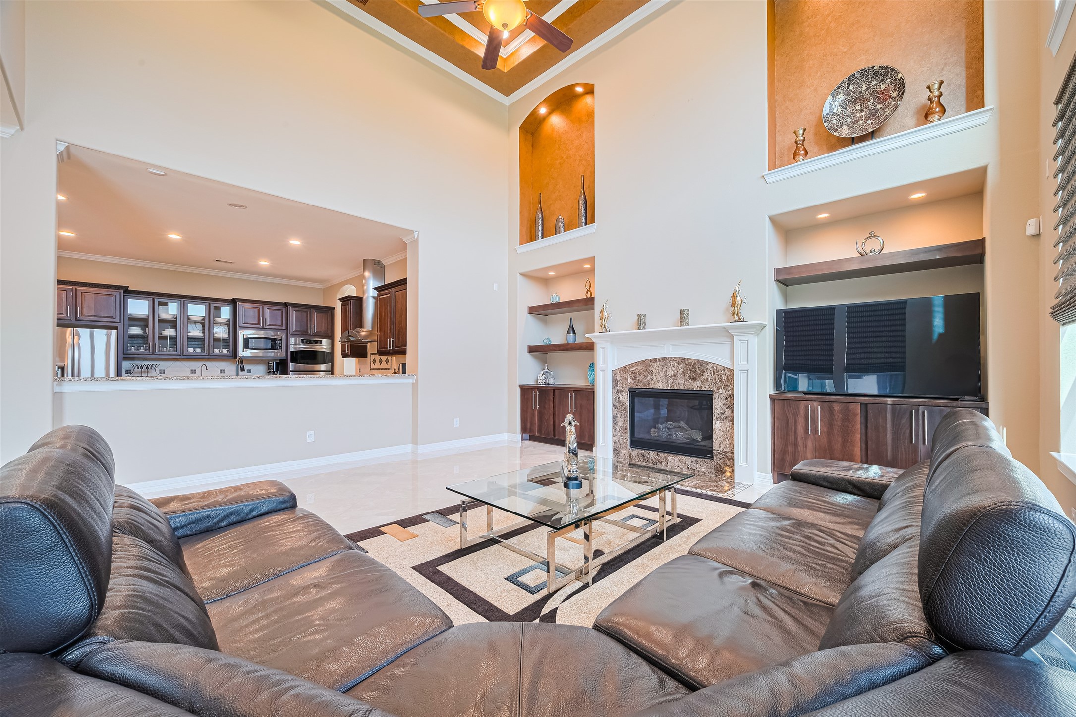 Reverse family room view showcasing the fireplace surround, illuminated display niches, built-in entertainment center, and open connection to the kitchen.