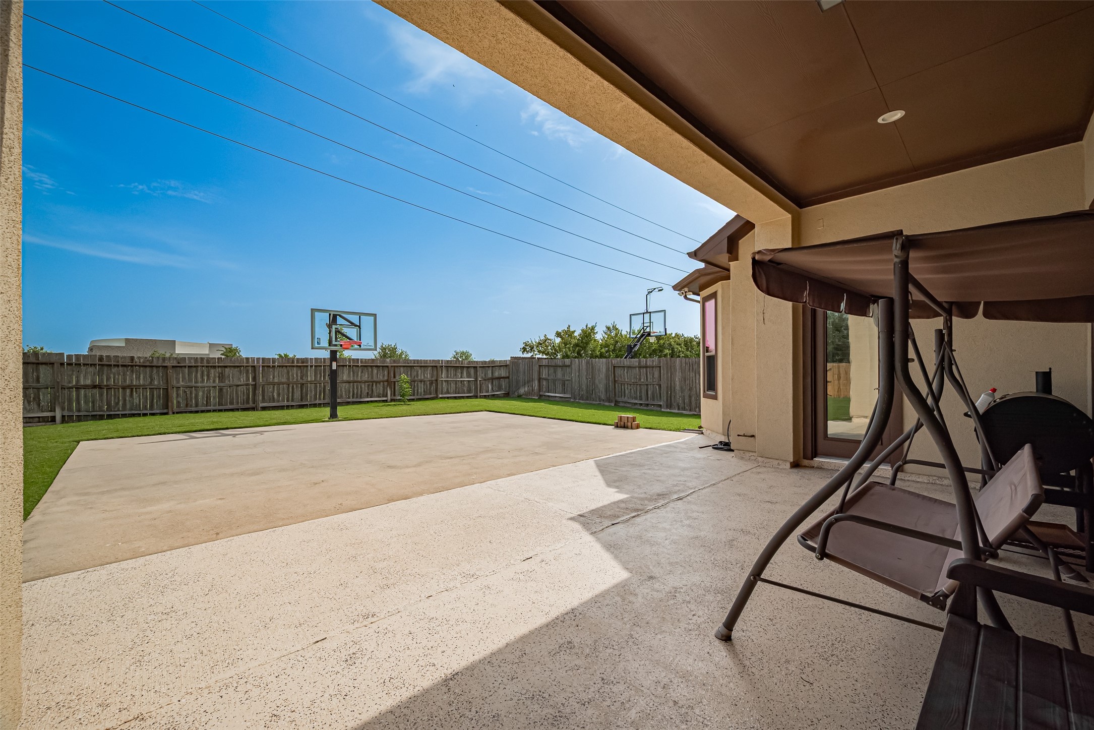 Spacious covered patio overlooking a large fenced backyard with an expansive concrete play area and basketball hoopsideal for outdoor recreation and entertaining.