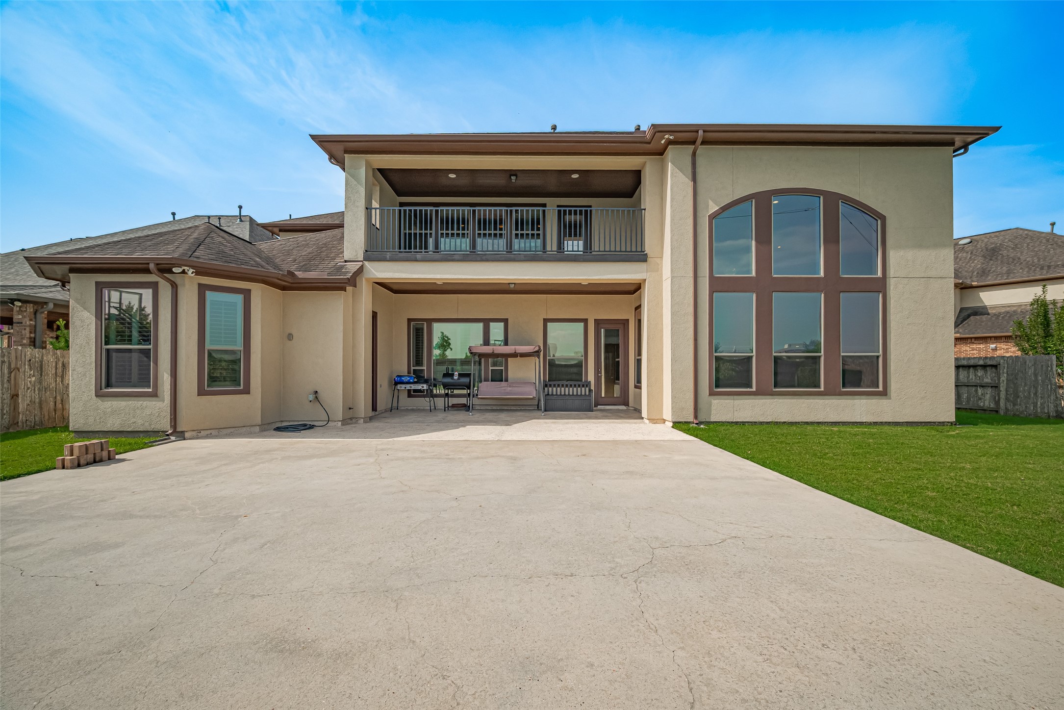 Striking rear elevation featuring a spacious covered patio, private upper balcony, expansive windows, and a large concrete recreation area ideal for outdoor entertaining.