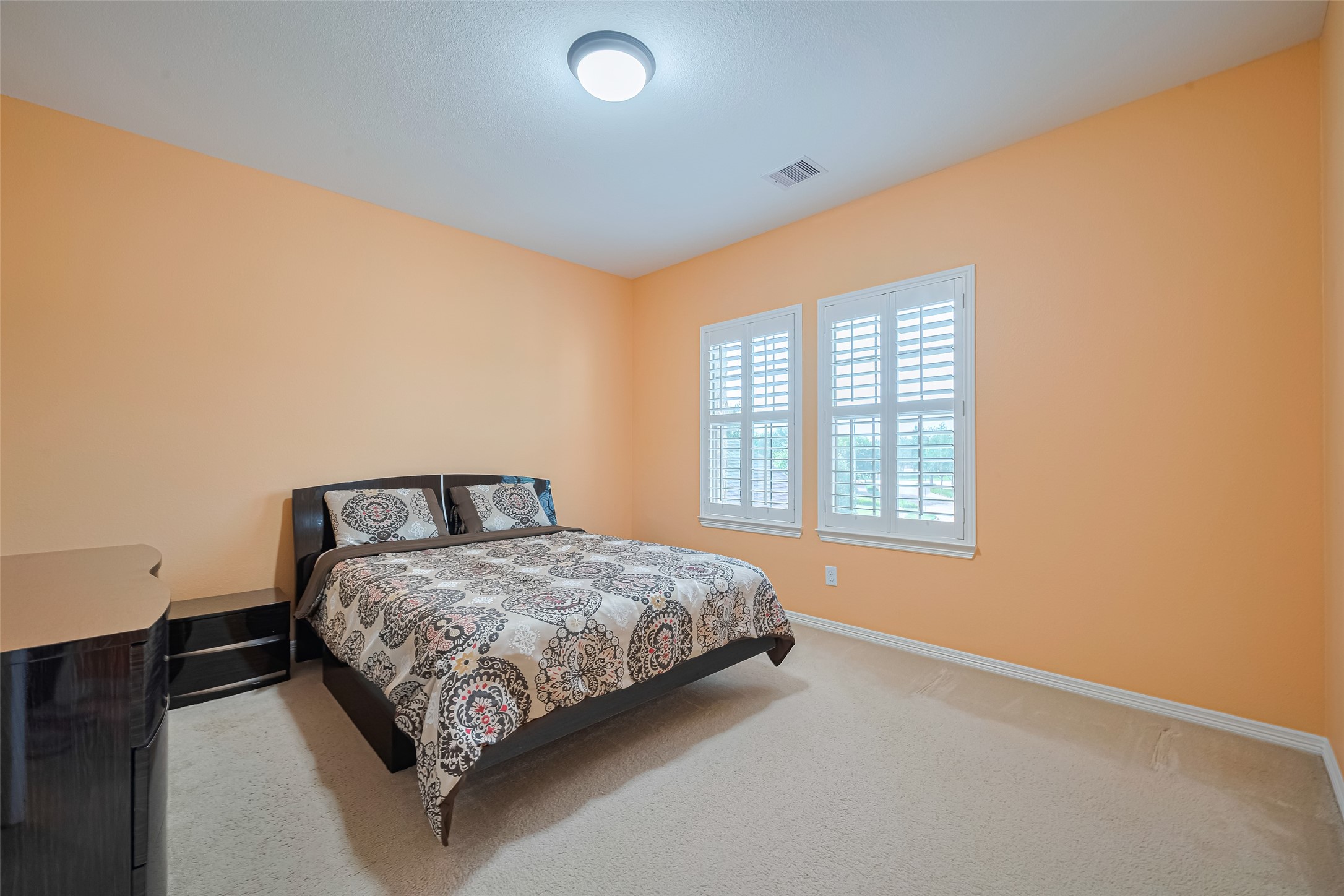 Spacious fourth bedroom featuring warm tones, plush carpeting, generous natural light, and ample room for comfortable furnishings.