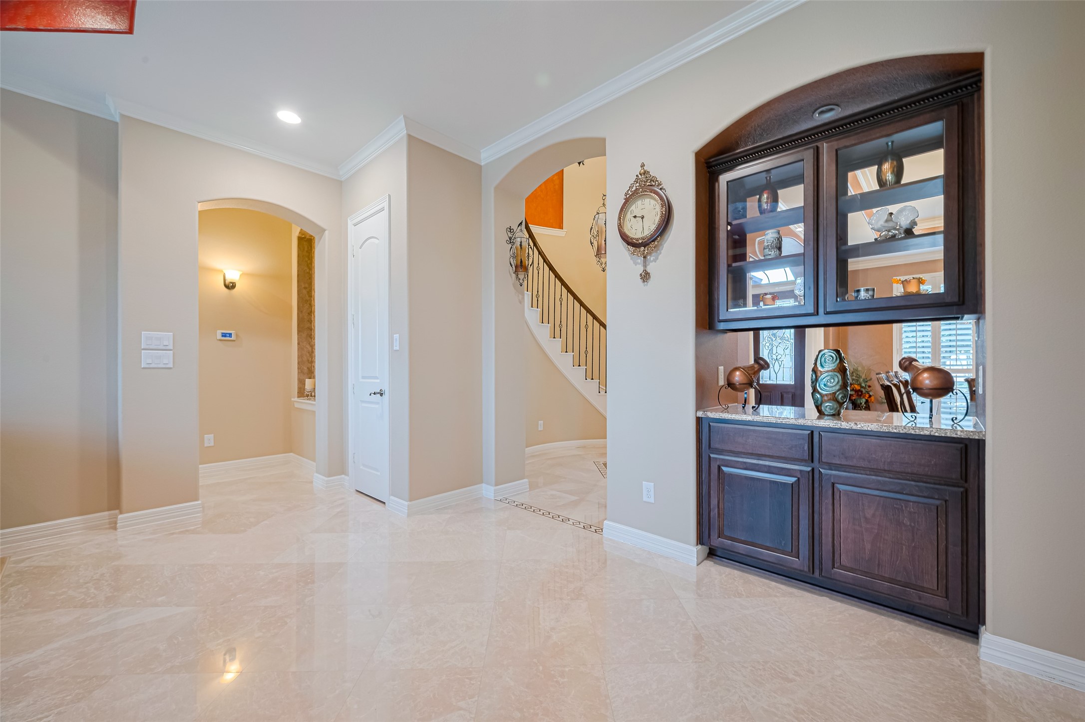 Convenient built-in serving bar with glass-front cabinetry, granite counter, and mirrored backsplash connecting the main entertaining spaces.