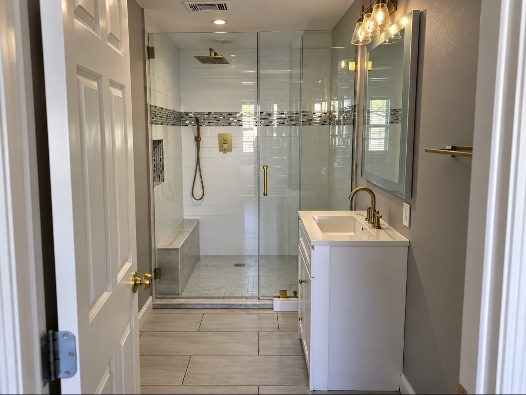 Modern bathroom featuring a spacious glass-enclosed shower with stylish tile accents and a sleek vanity with gold fixtures for a touch of elegance.