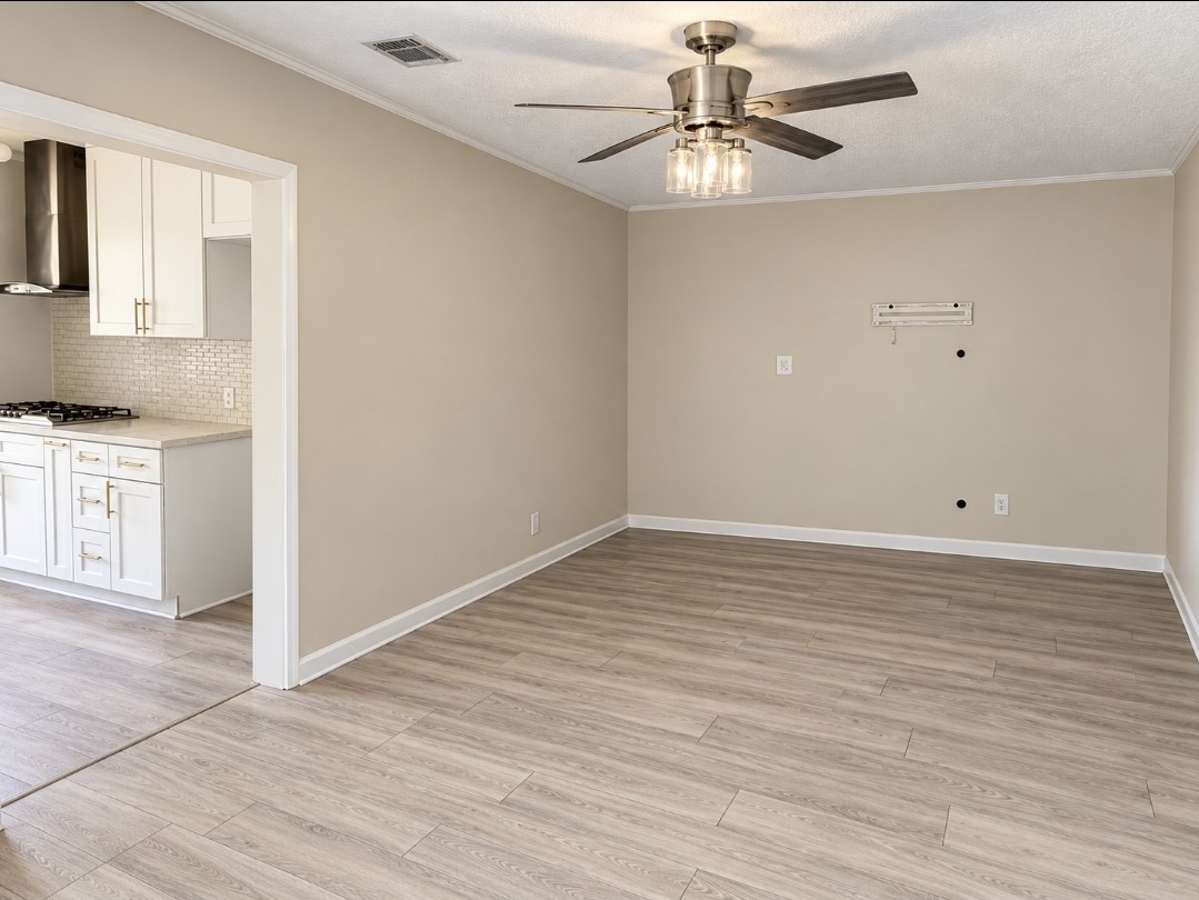 Bright and inviting living space with modern wood flooring, a stylish ceiling fan, and an adjoining kitchen featuring sleek white cabinetry and stainless steel appliances.