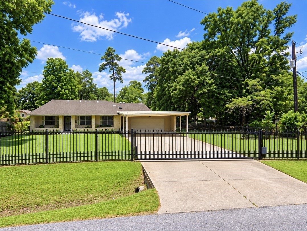 Charming single-story home with a spacious front yard, secure gated driveway, and ample carport, nestled among mature trees for added privacy and tranquility.