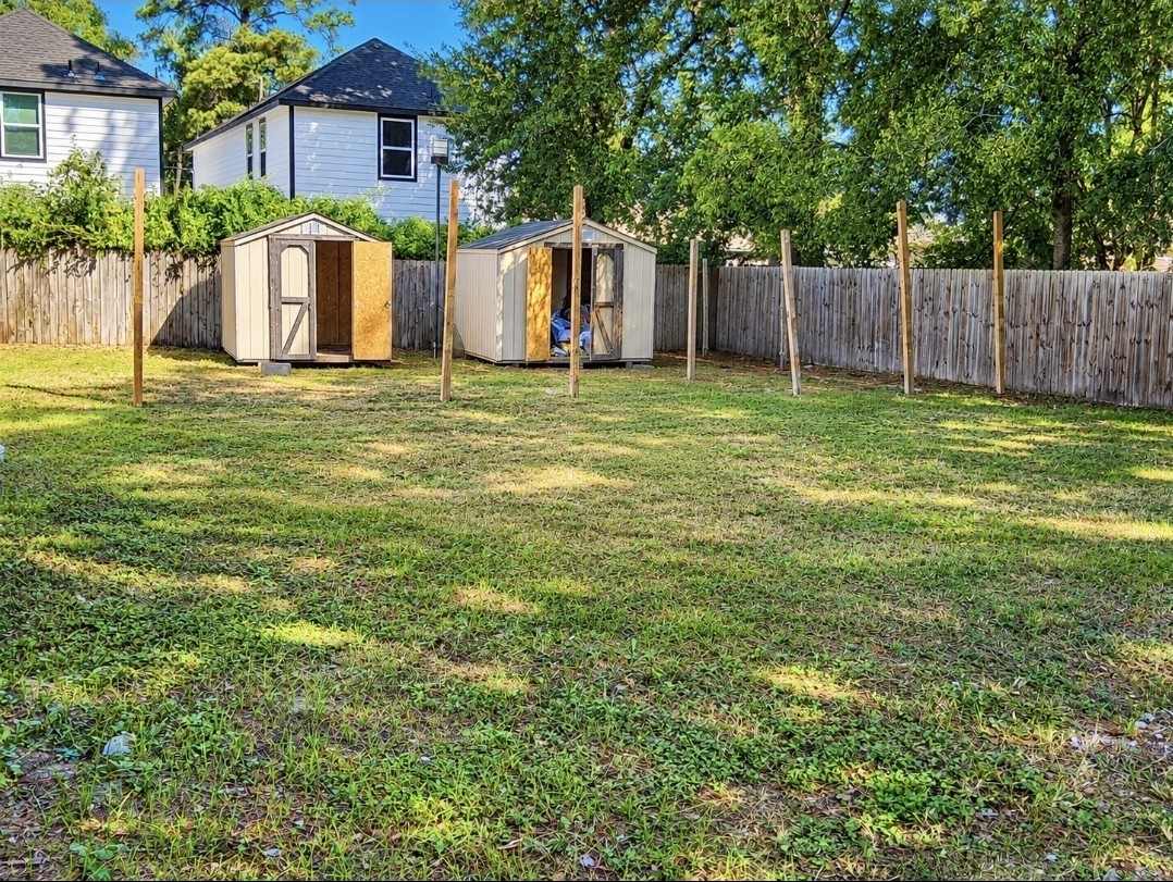 Spacious backyard with lush grass, fenced for privacy, featuring two storage sheds and surrounded by mature trees.