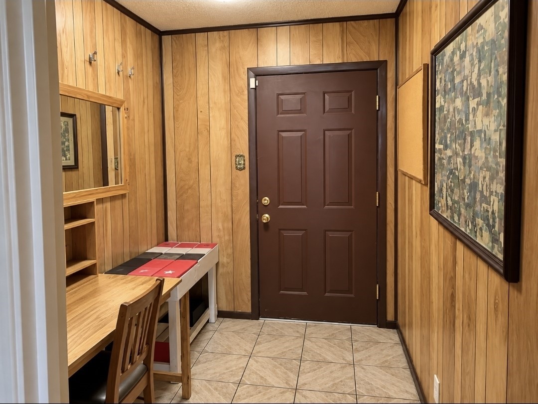 Cozy entryway featuring warm wood paneling, a functional desk area, and a decorative tiled floor, offering a welcoming first impression.