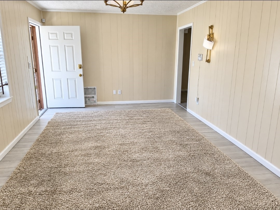 Bright, welcoming room with light wood-paneled walls, plush carpet, and a stylish chandelier, offering a cozy and inviting atmosphere.