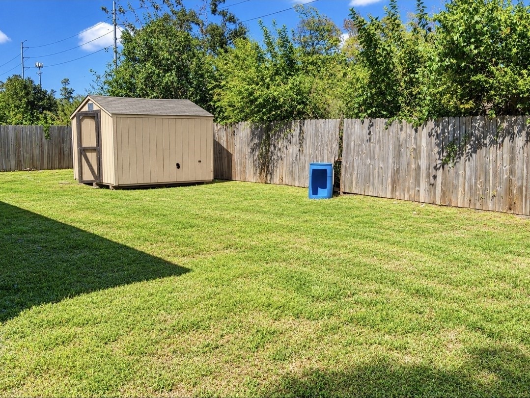 Spacious backyard with lush green lawn, a sturdy wooden fence for privacy, and a practical storage shed for extra space.