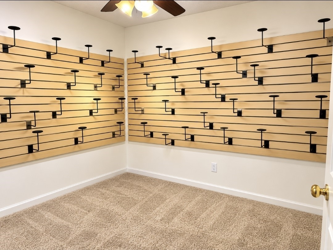 Versatile room featuring slatwall panels with adjustable brackets, perfect for customizable storage or display, complemented by cozy carpet flooring and a ceiling fan.