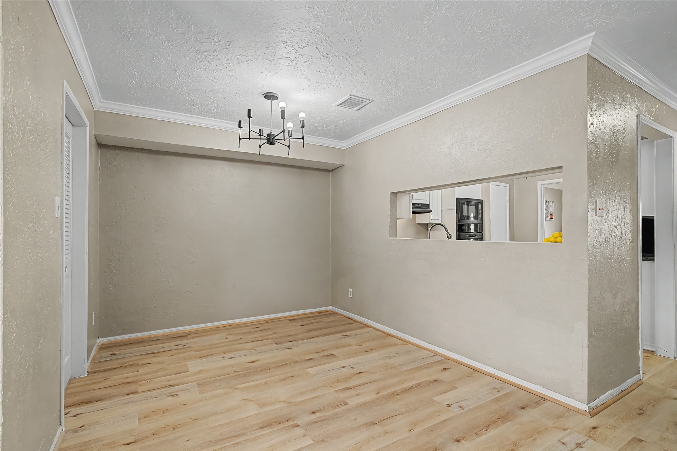 Open breakfast room with wood-look flooring, crown molding, and a pass-through opening to the kitchen.
