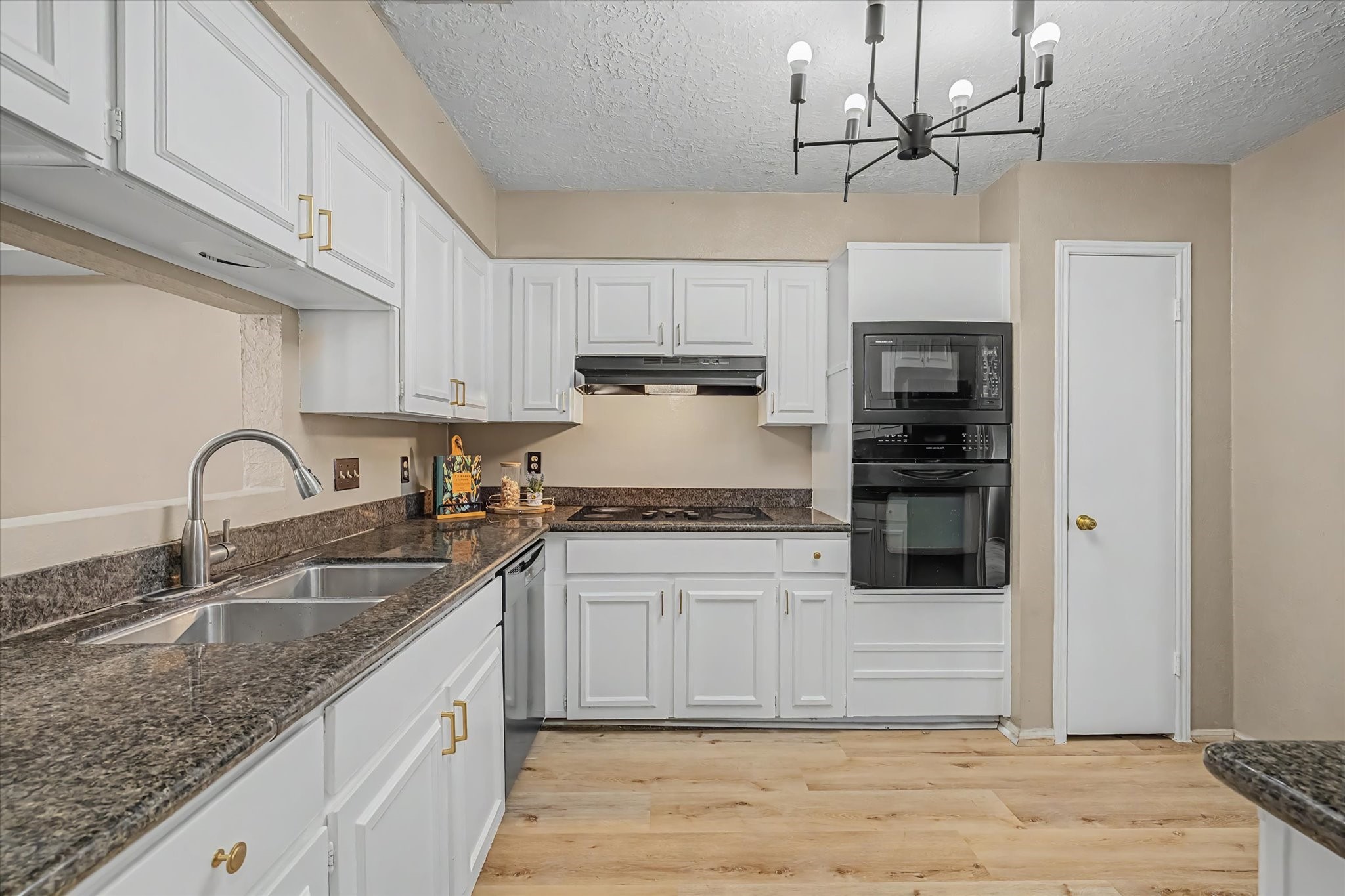 Kitchen featuring white cabinetry, granite countertops, double-basin sink, built-in appliances, and wood-look flooring.