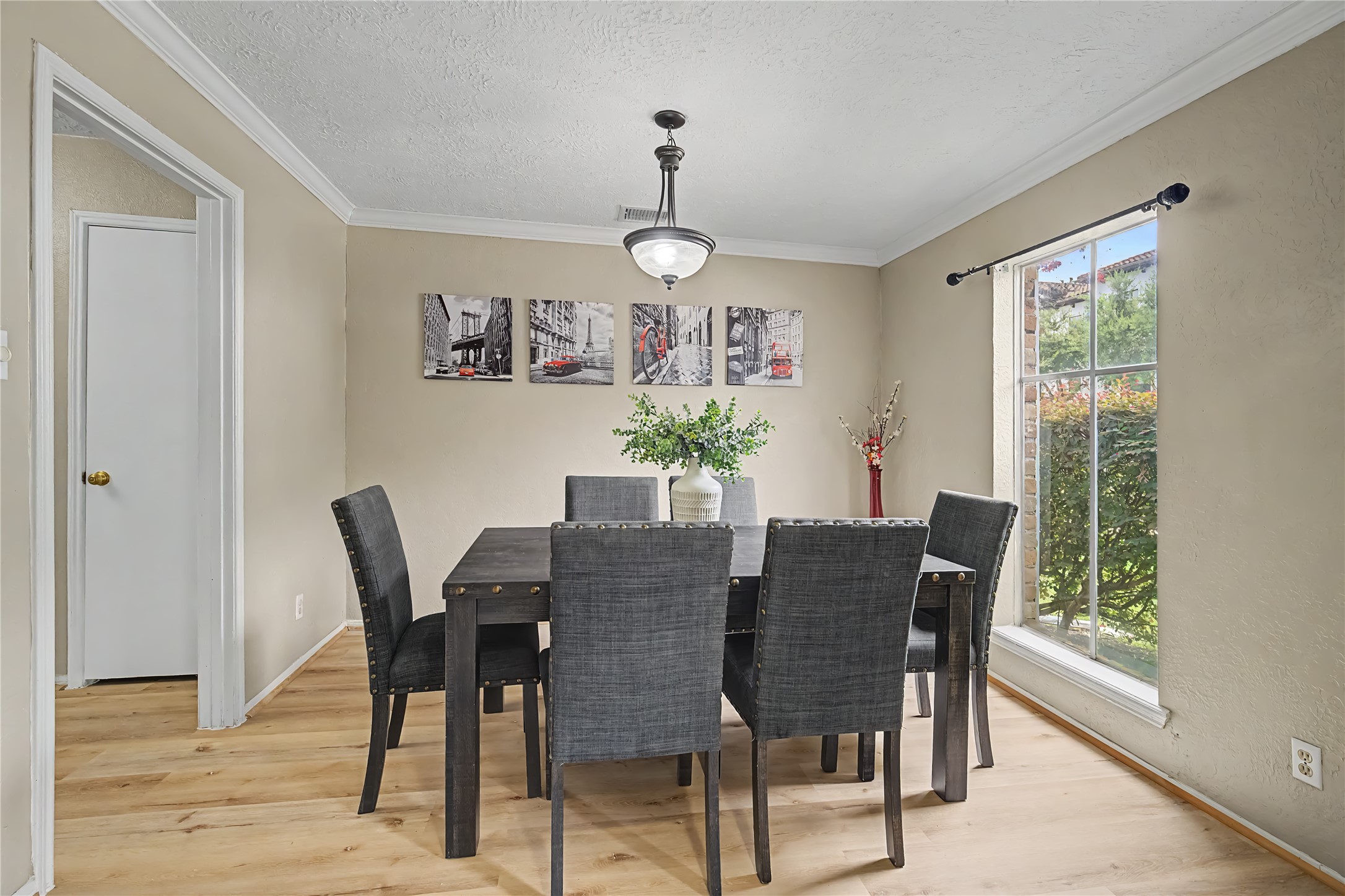 Spacious dining area with wood-look flooring, crown molding, overhead lighting, and a large window.