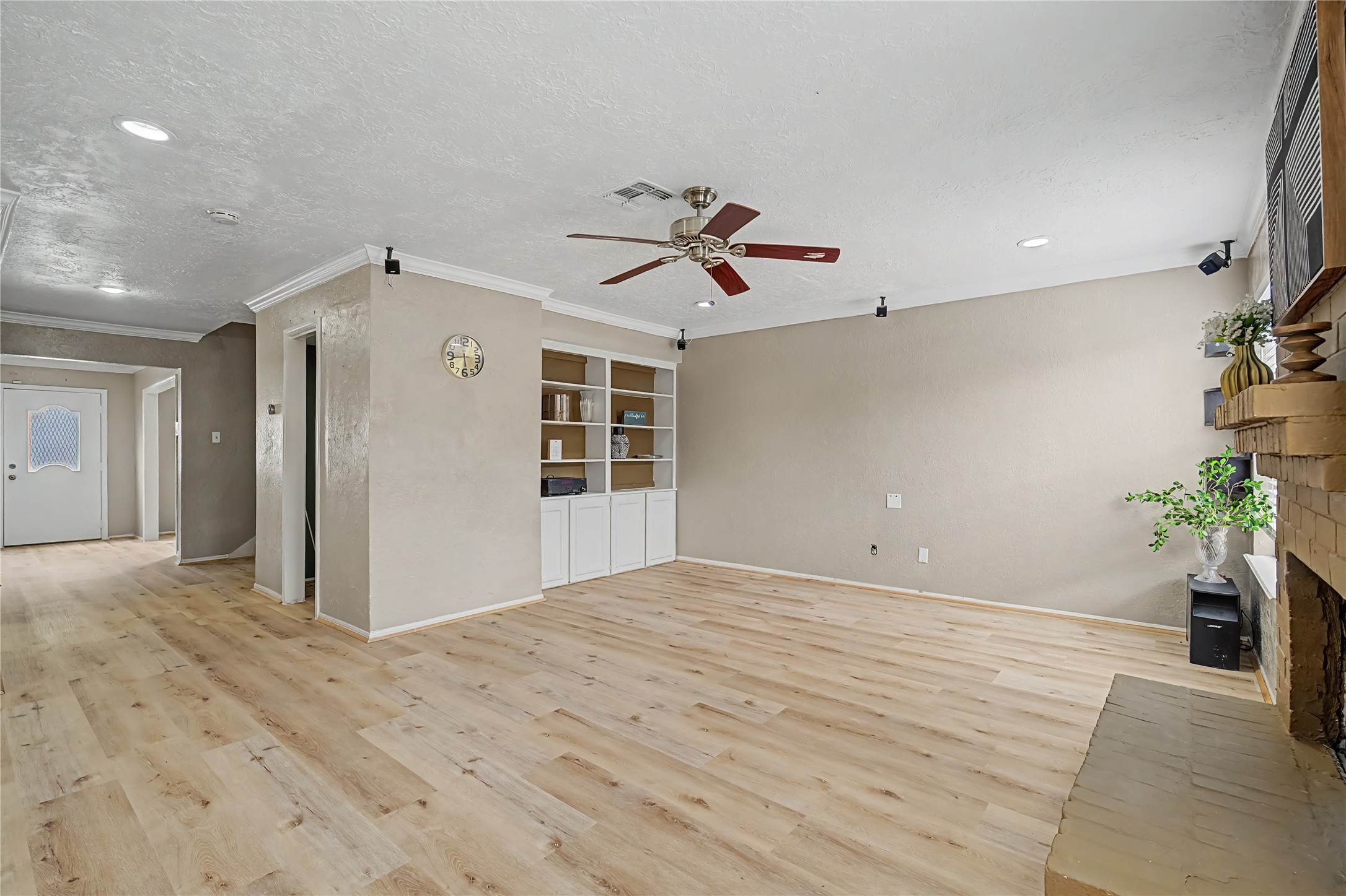 Spacious living area with wood-look flooring, recessed lighting, ceiling fan, and a brick fireplace.
