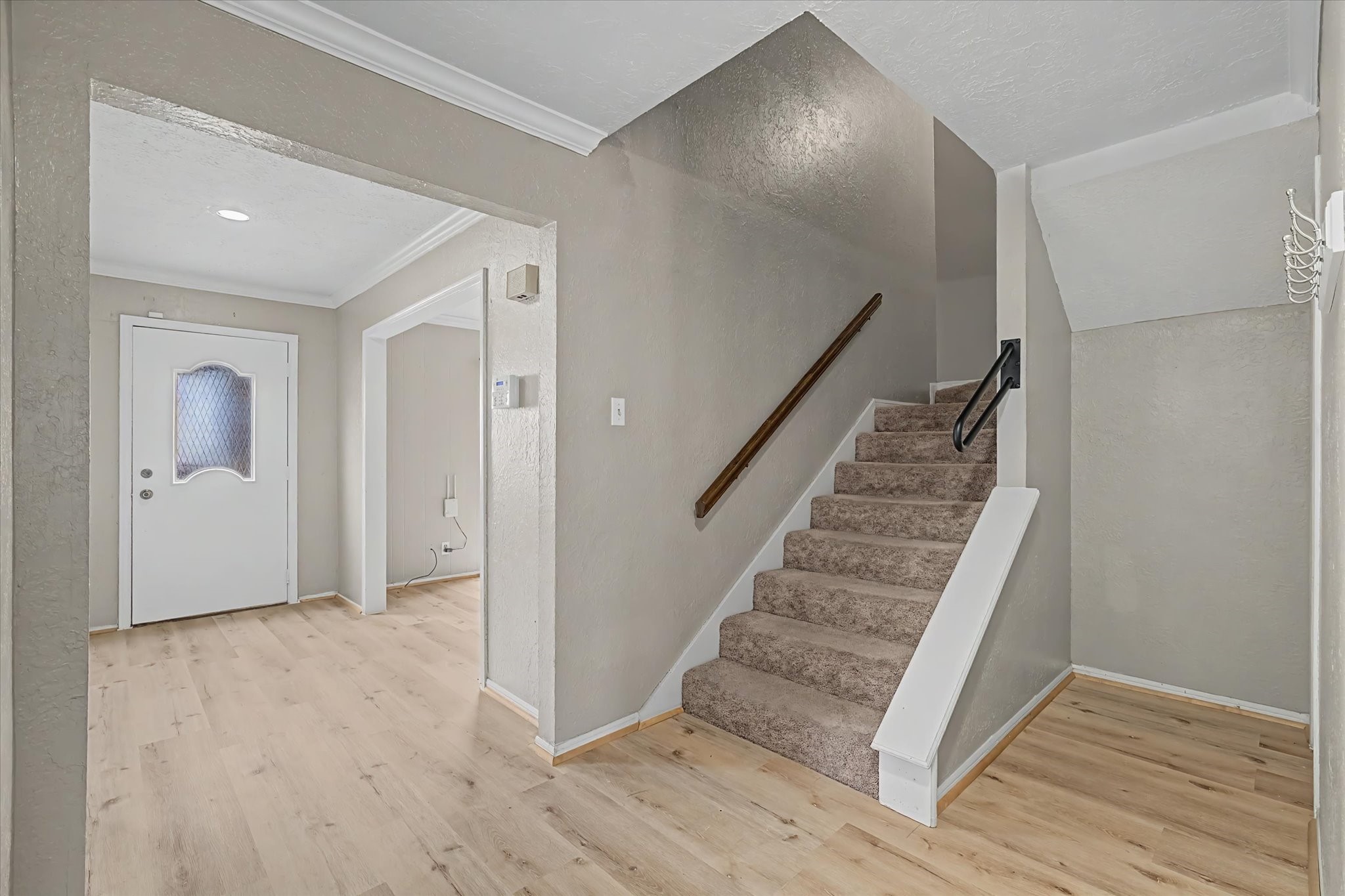 Bright entryway with wood-look flooring and carpeted staircase leading upstairs.