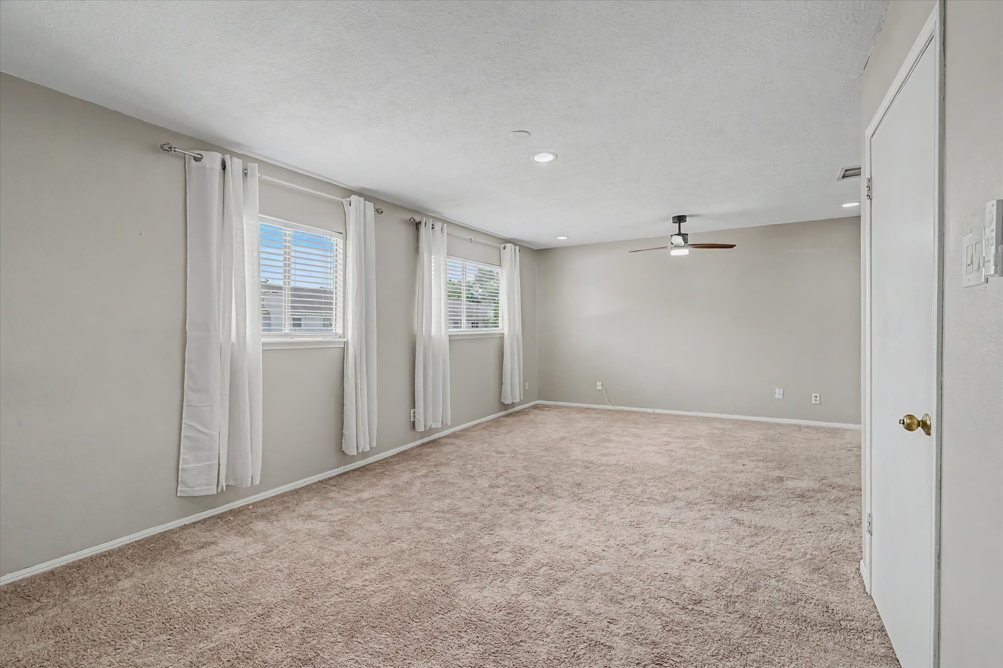 Generously sized primary bedroom with neutral carpeting, recessed lighting, ceiling fan, and multiple windows for natural light.