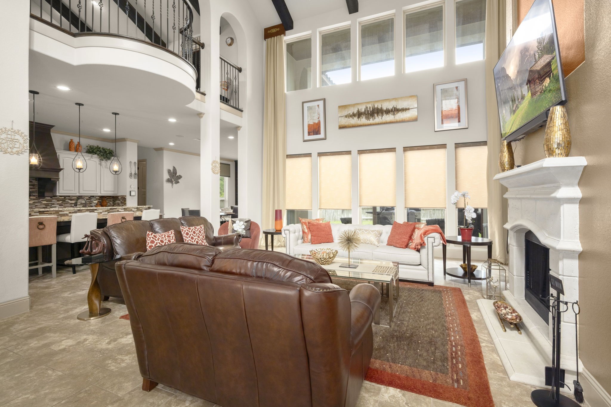 This spacious living room features high ceilings, large windows with abundant natural light, and a central fireplace. The open layout connects to the kitchen area, enhancing the sense of space.
