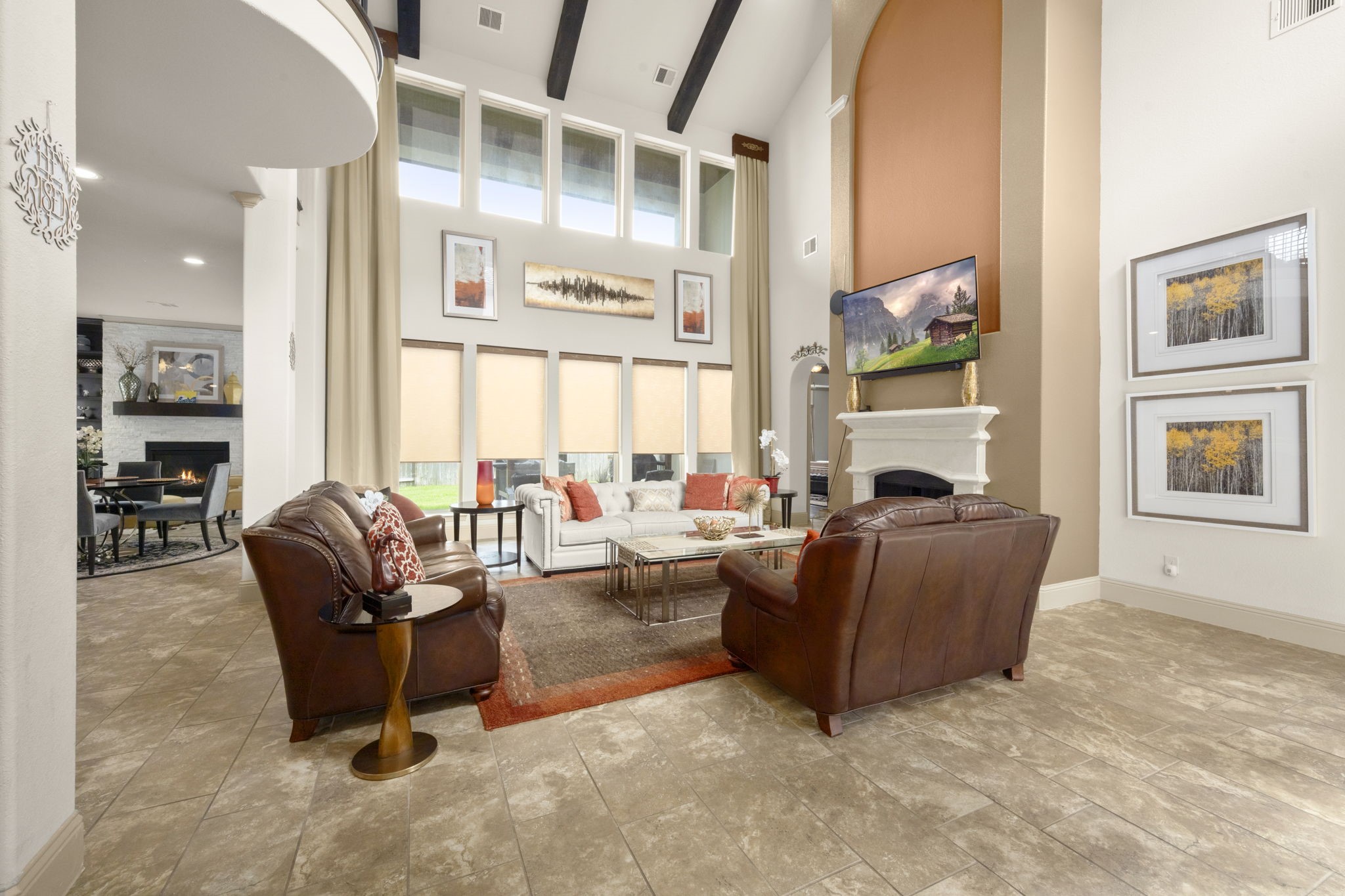 This spacious living room features high ceilings, large windows with abundant natural light, and a central fireplace. The open layout connects to the kitchen area, enhancing the sense of space.