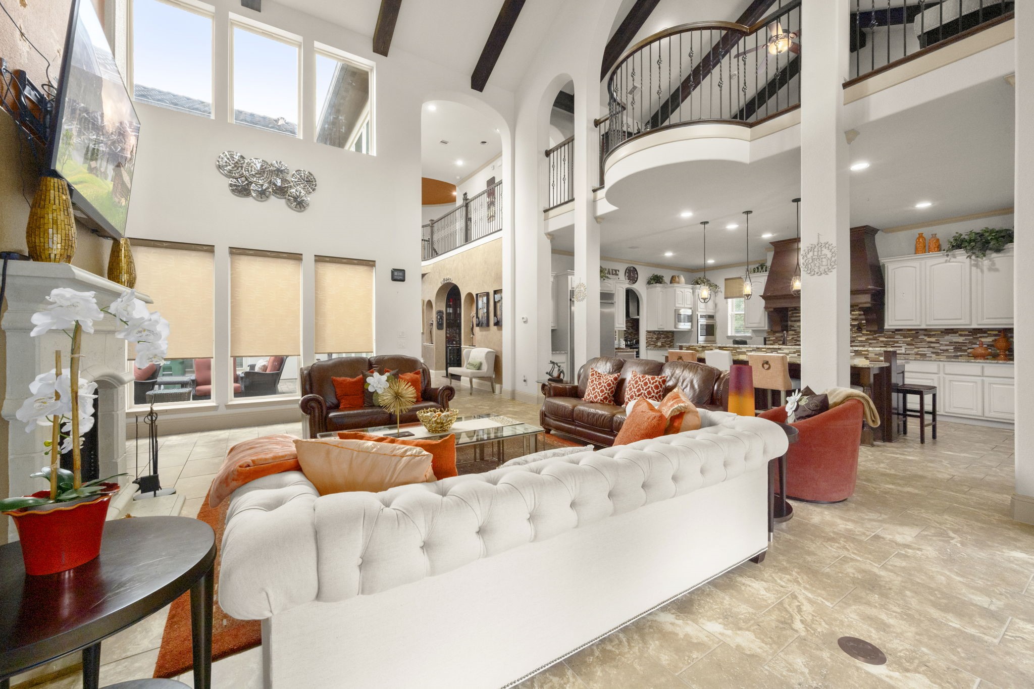 This spacious living room features high ceilings, large windows with abundant natural light, and a central fireplace. The open layout connects to the kitchen area, enhancing the sense of space.