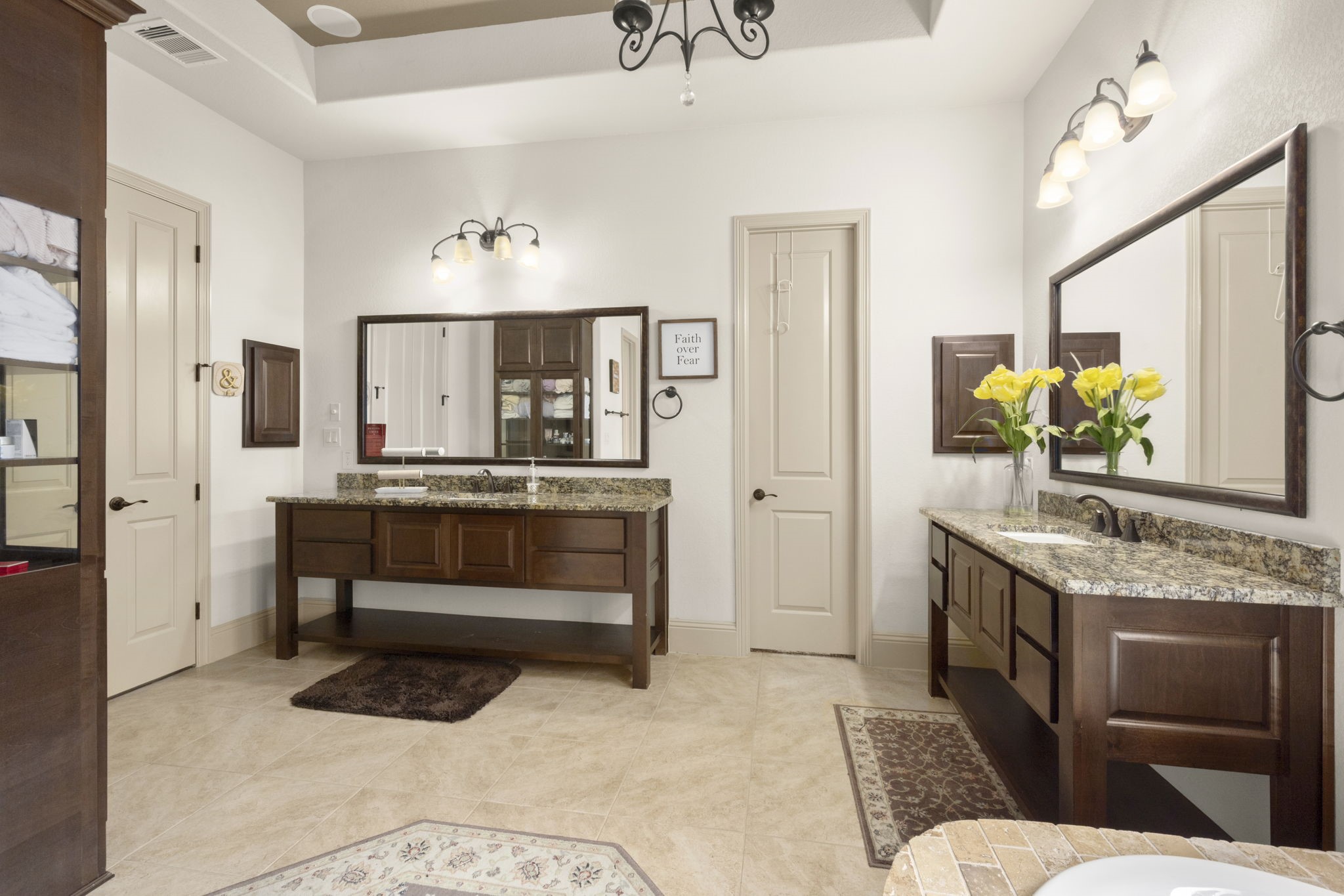 This spacious bathroom features dual vanities with granite countertops, elegant lighting fixtures, and ample cabinet storage. It also features a shower, tub and two walk-in closets.