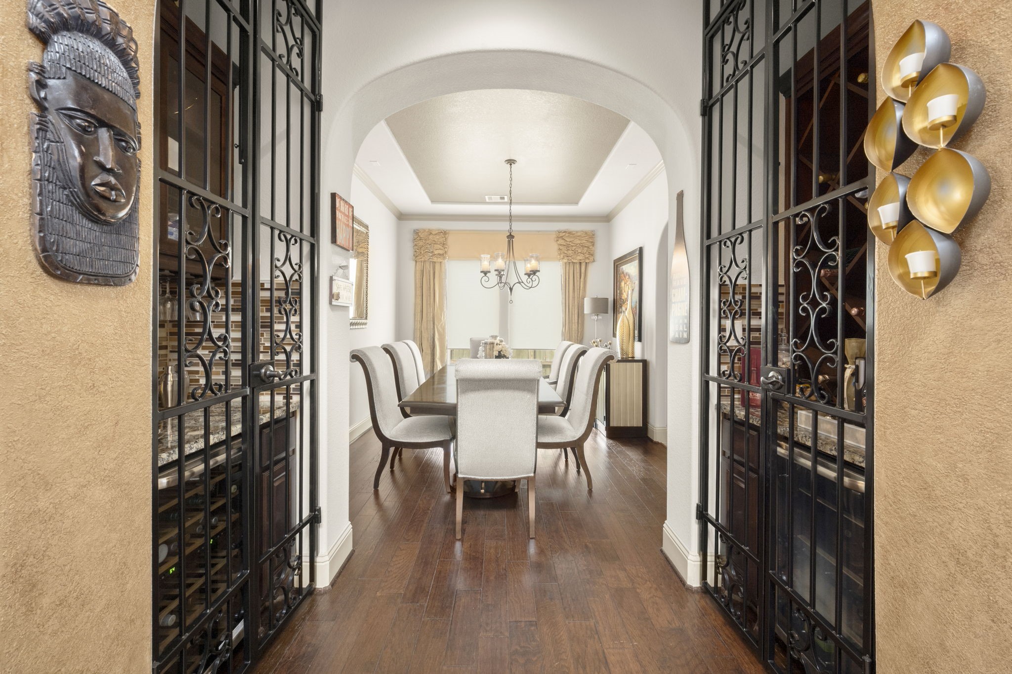 A designated dining area with rich wooden flooring and a sophisticated chandelier. The entryway of the room features a bar and wine cabinet framed by decorative iron gates.