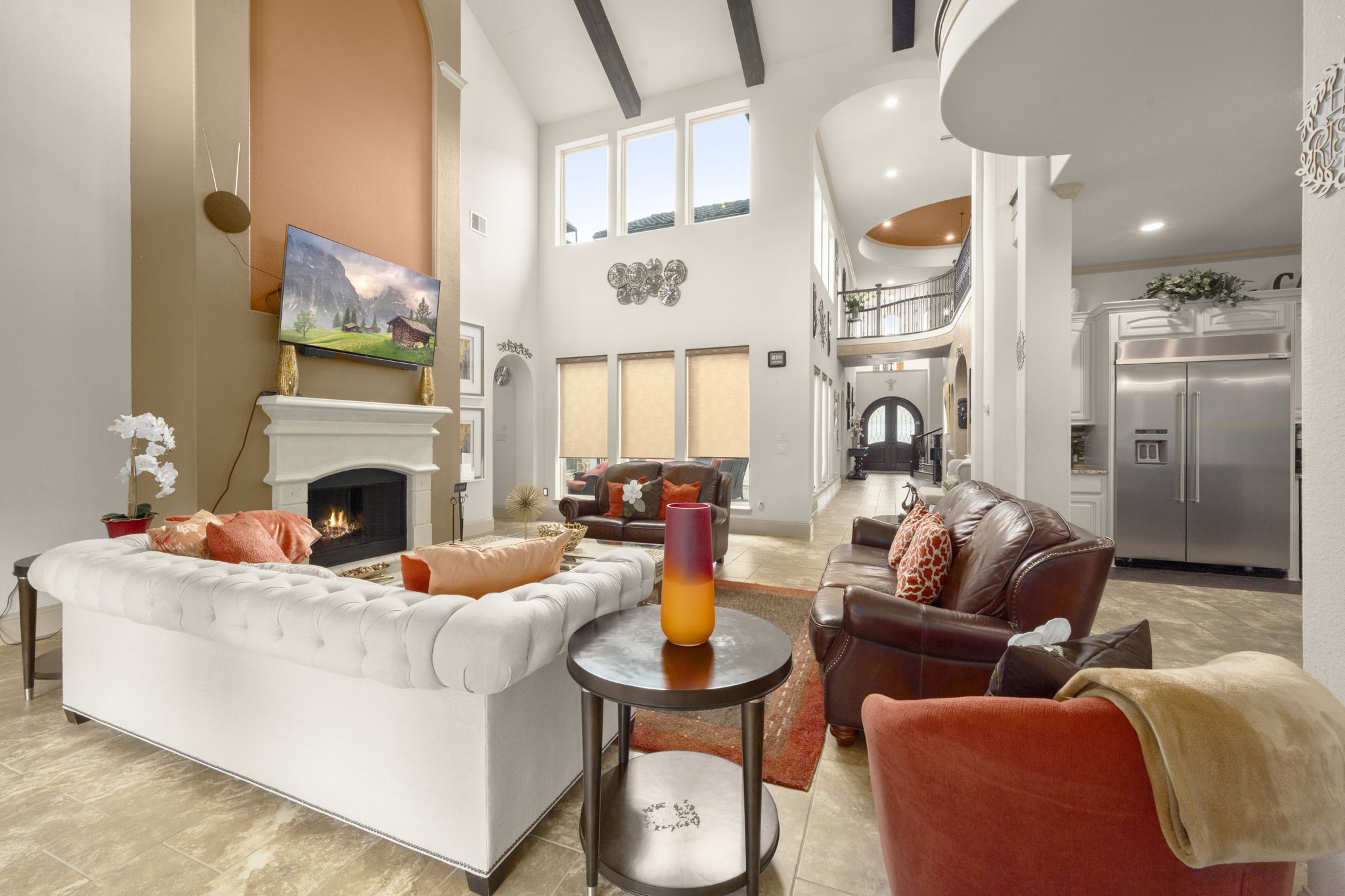 This spacious living room features high ceilings, large windows with abundant natural light, and a central fireplace. The open layout connects to the kitchen area, enhancing the sense of space.