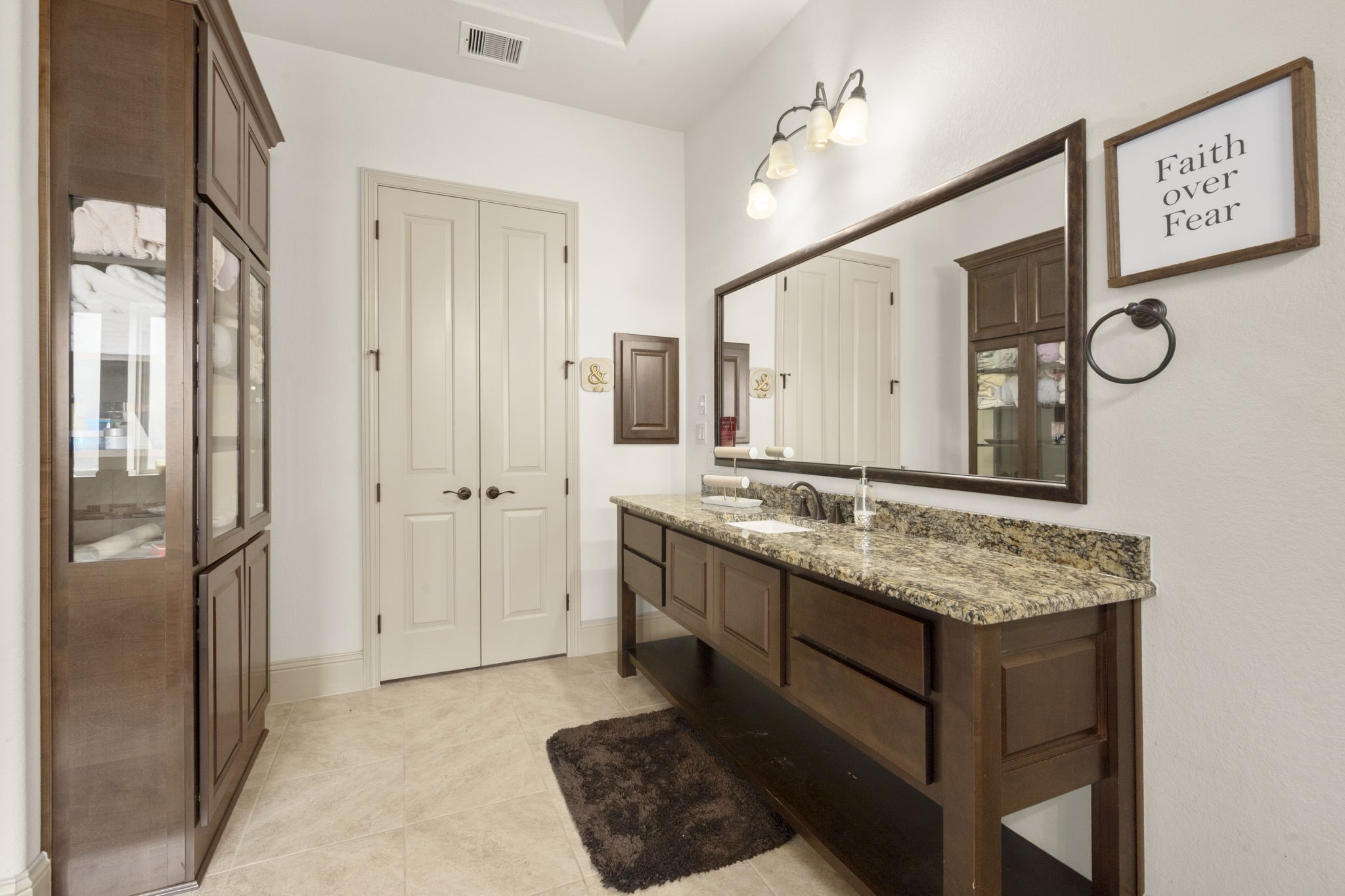 This spacious bathroom features dual vanities with granite countertops, elegant lighting fixtures, and ample cabinet storage. It also features a shower, tub and two walk-in closets.