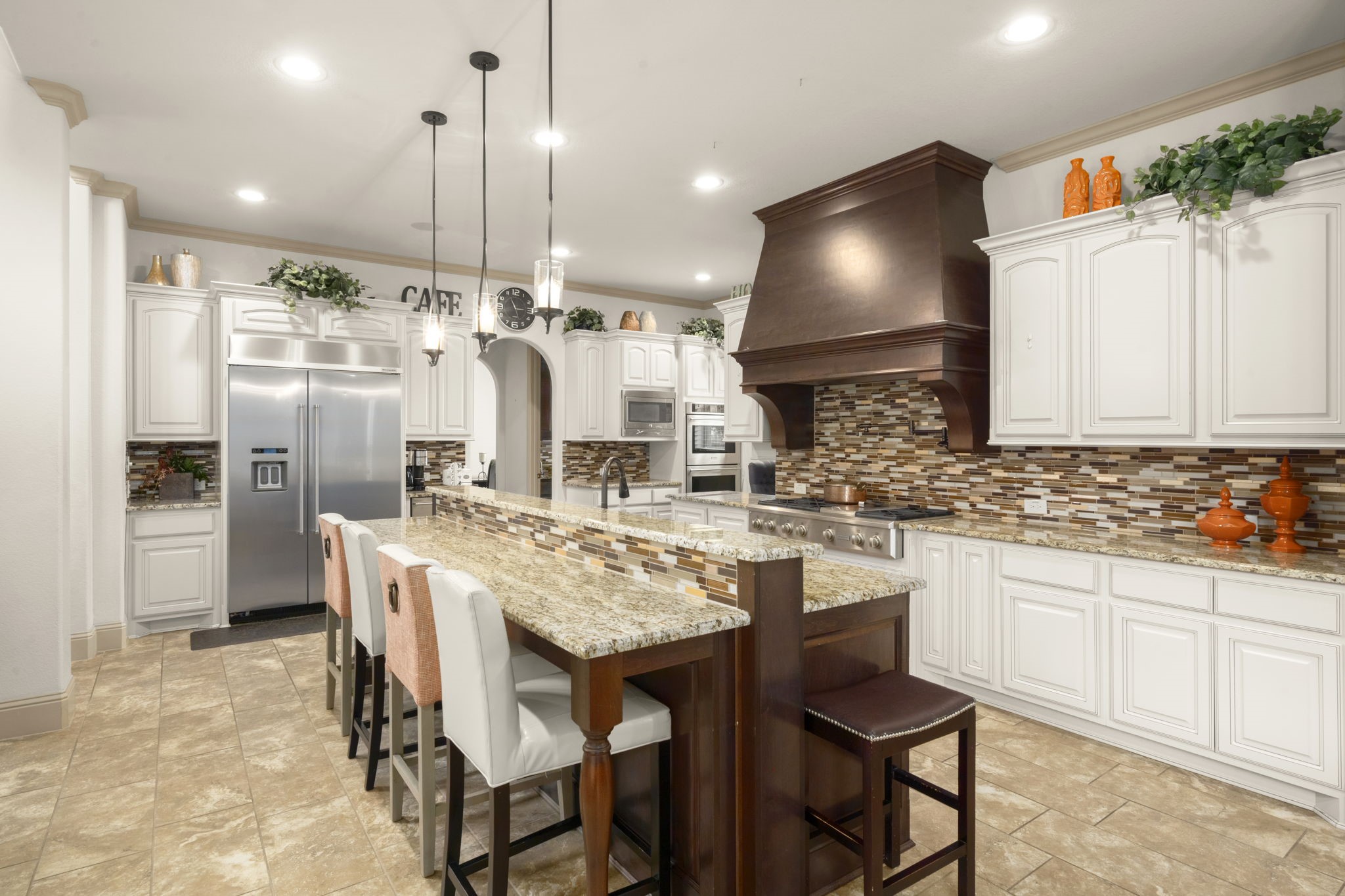 This modern kitchen includes stainless steel appliances, a large island with stylish pendant lighting, a spacious breakfast bar, a walk-in pantry and a secondary kitchenette.