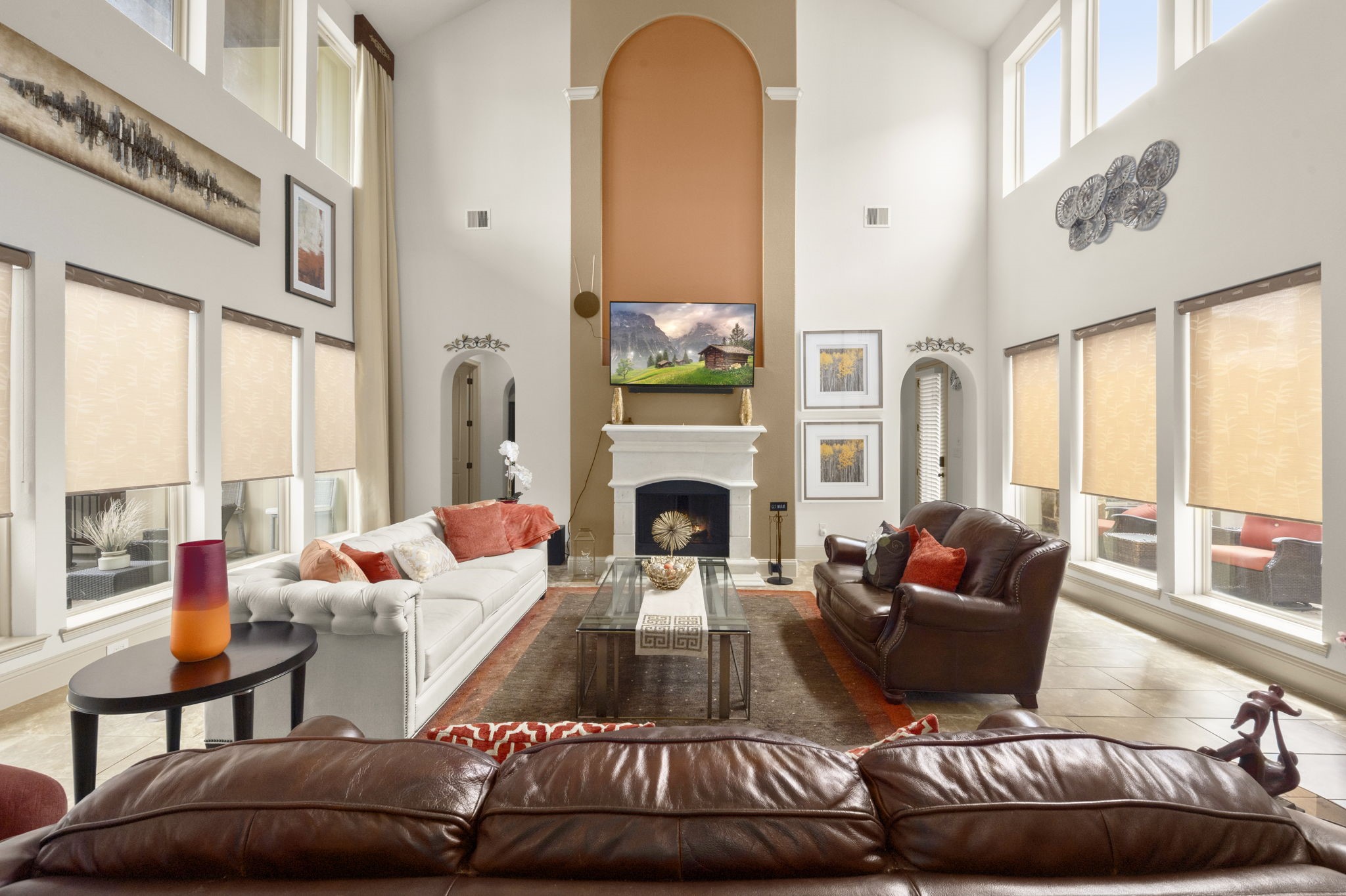 This spacious living room features high ceilings, large windows with abundant natural light, and a central fireplace. This space creates an inviting atmosphere perfect for relaxation and entertainment.