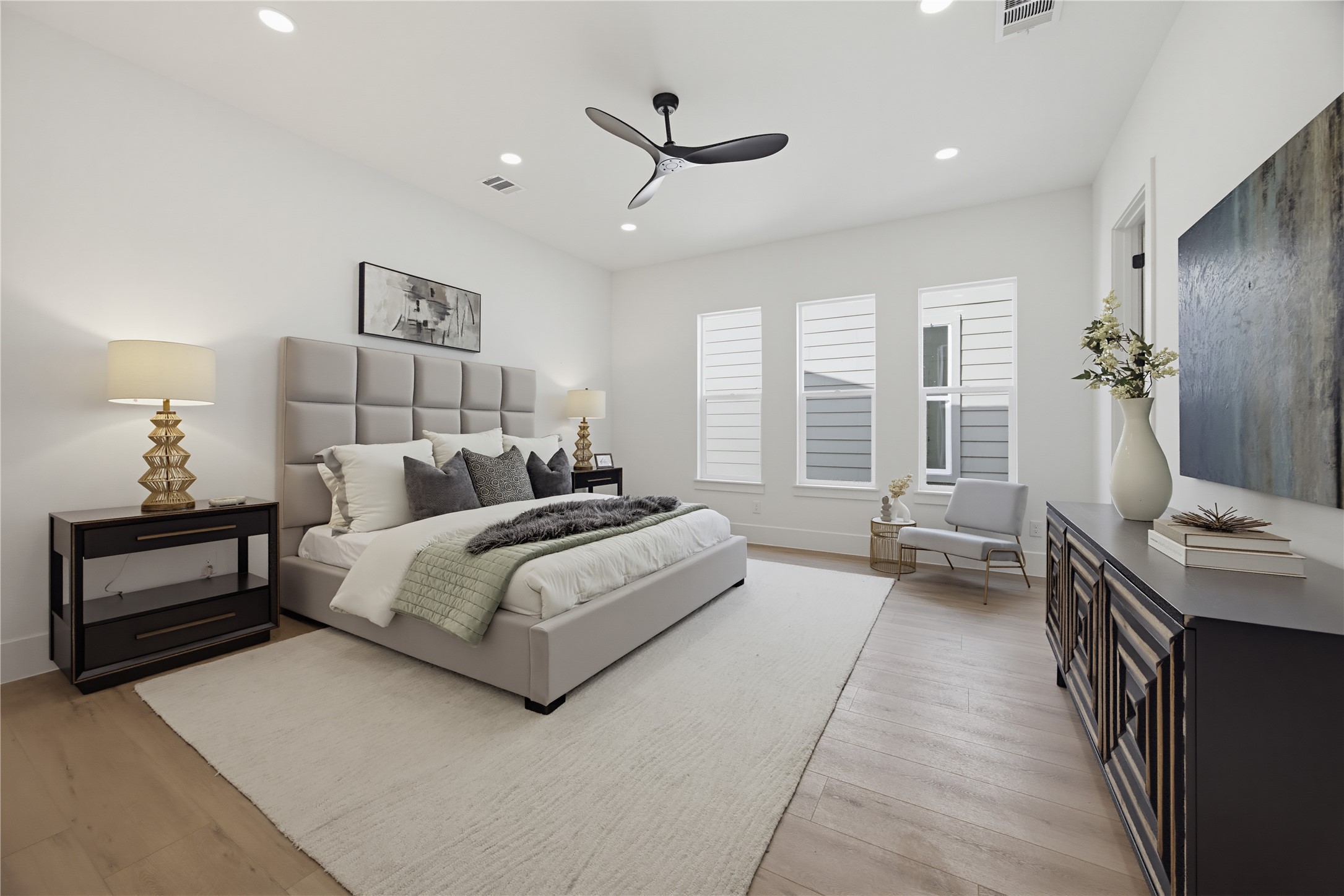 Elegant and spacious primary bedroom. Natural light pours in through tall windows, highlighting the serene ambiance.