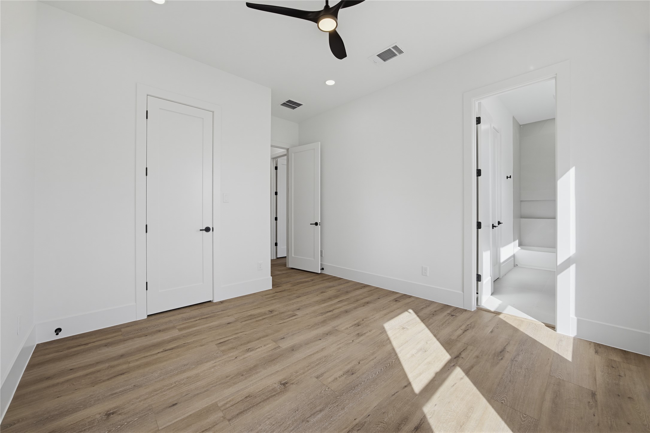 Bright and airy 2nd bedroom featuring sleek hardwood floors, modern ceiling fan, and ample natural light, with convenient access to an ensuite bathroom.