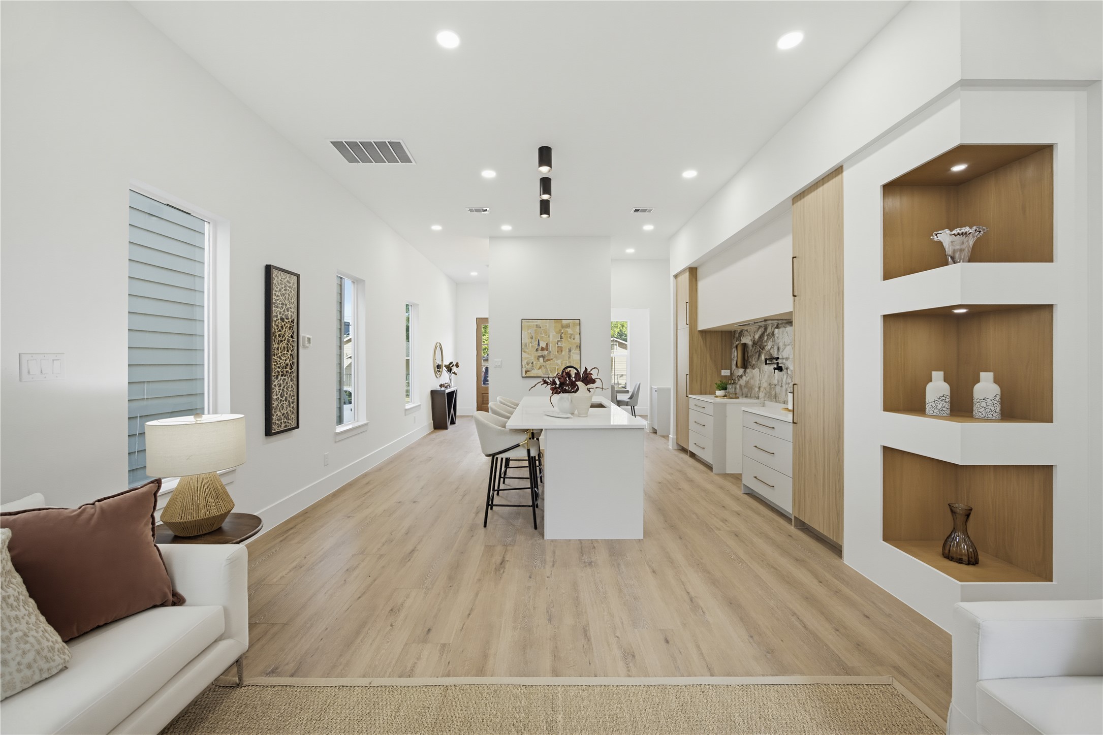 Sleek and modern open-concept living space with elegant wood flooring, built-in shelving, and a stylish kitchen featuring a central island and contemporary cabinetry. Sleek and modern open-concept living space with elegant wood flooring, built-in shelving, and a stylish kitchen featuring a central island and contemporary cabinetry.