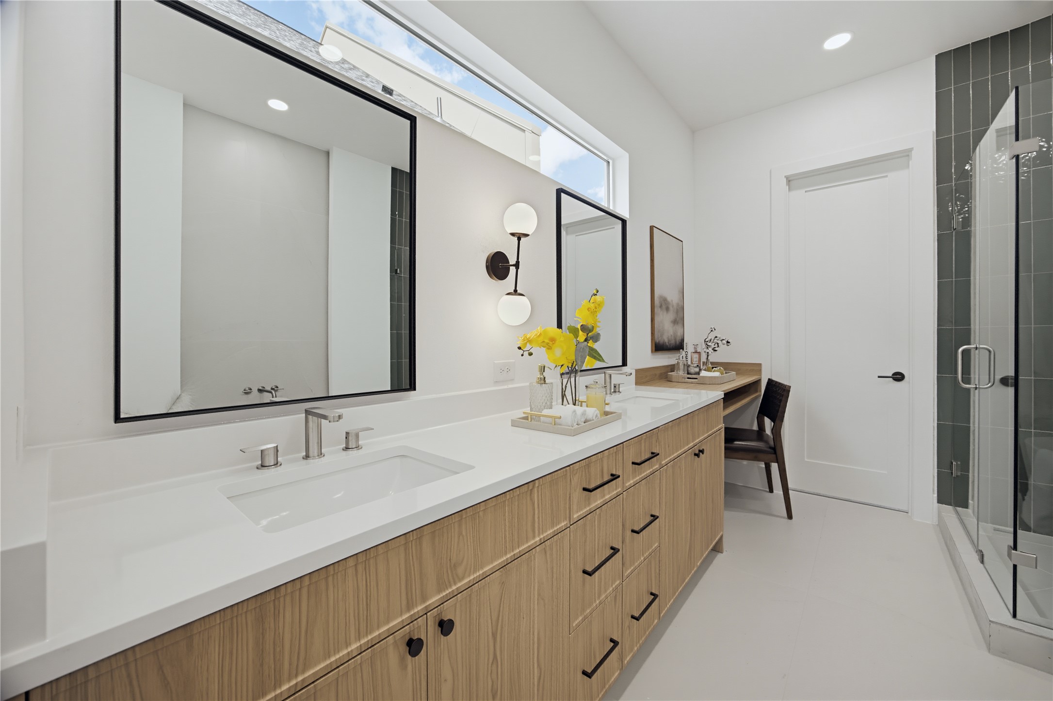 Elegant bathroom featuring a double vanity with sleek fixtures, ample storage, and a stylish glass-enclosed shower, complemented by modern lighting and a convenient makeup station.