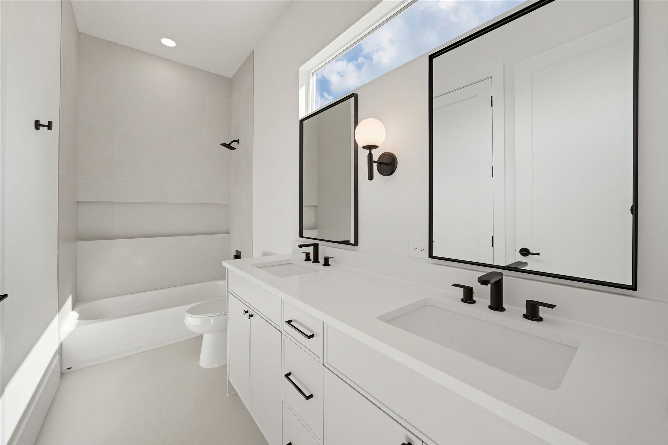 Sleek and modern bathroom featuring a double vanity with black fixtures, a spacious tub, and abundant natural light from a large window.