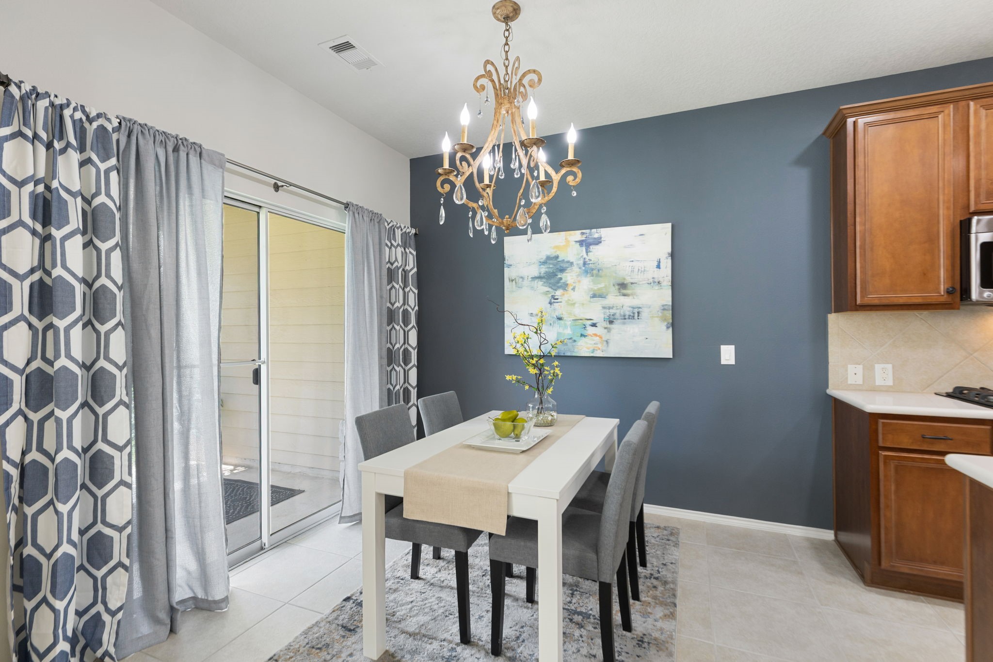The dining area is a gorgeous focal point with a modern vibe chandelier and a stylish blue accent wall, featuring a sliding glass door that opens to your covered patio.