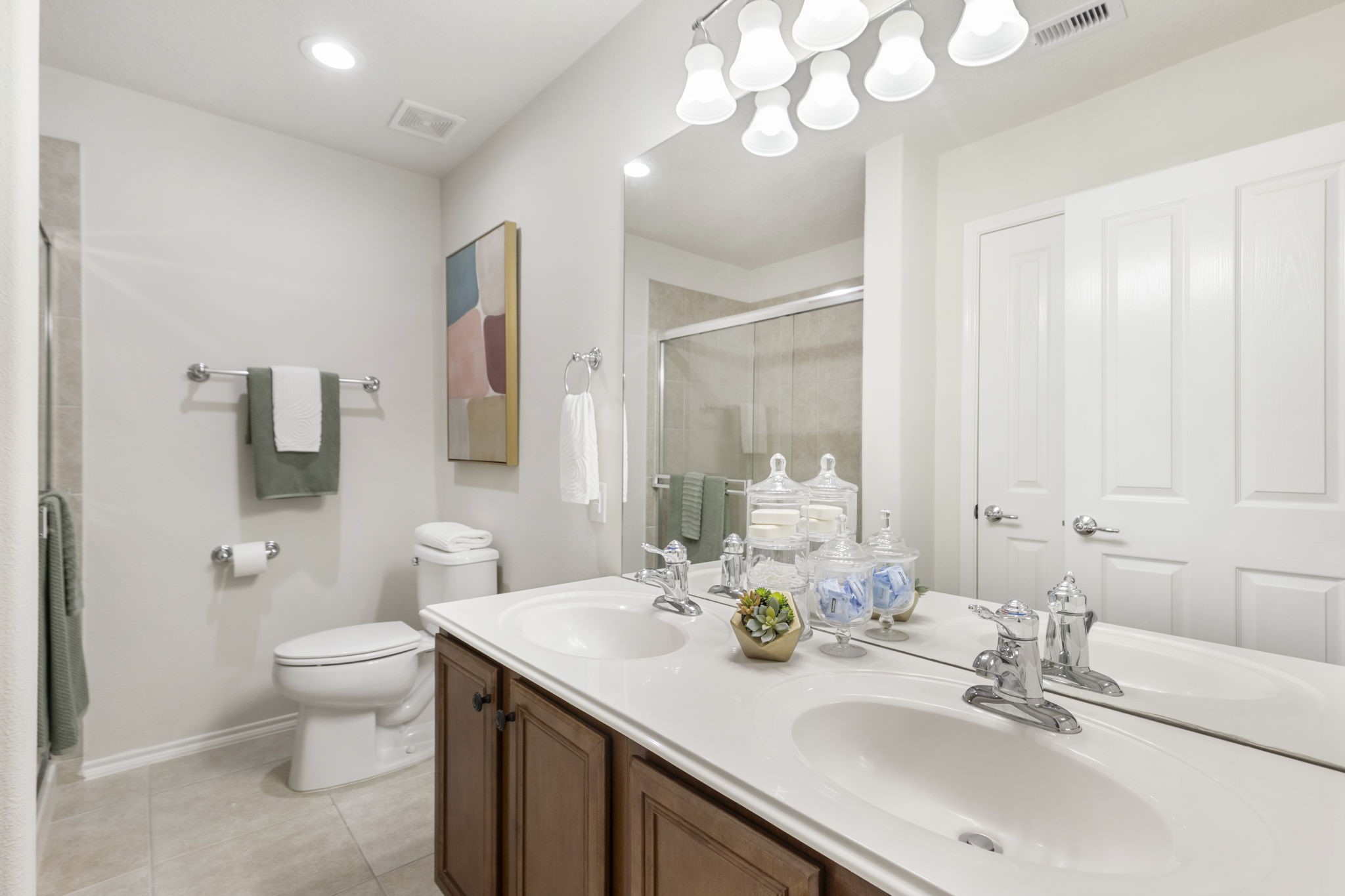 Your primary bathroom features a wide vanity with dual sinks, elegant fixtures, LED lighting, rich wood cabinetry and a generously sized storage closet.