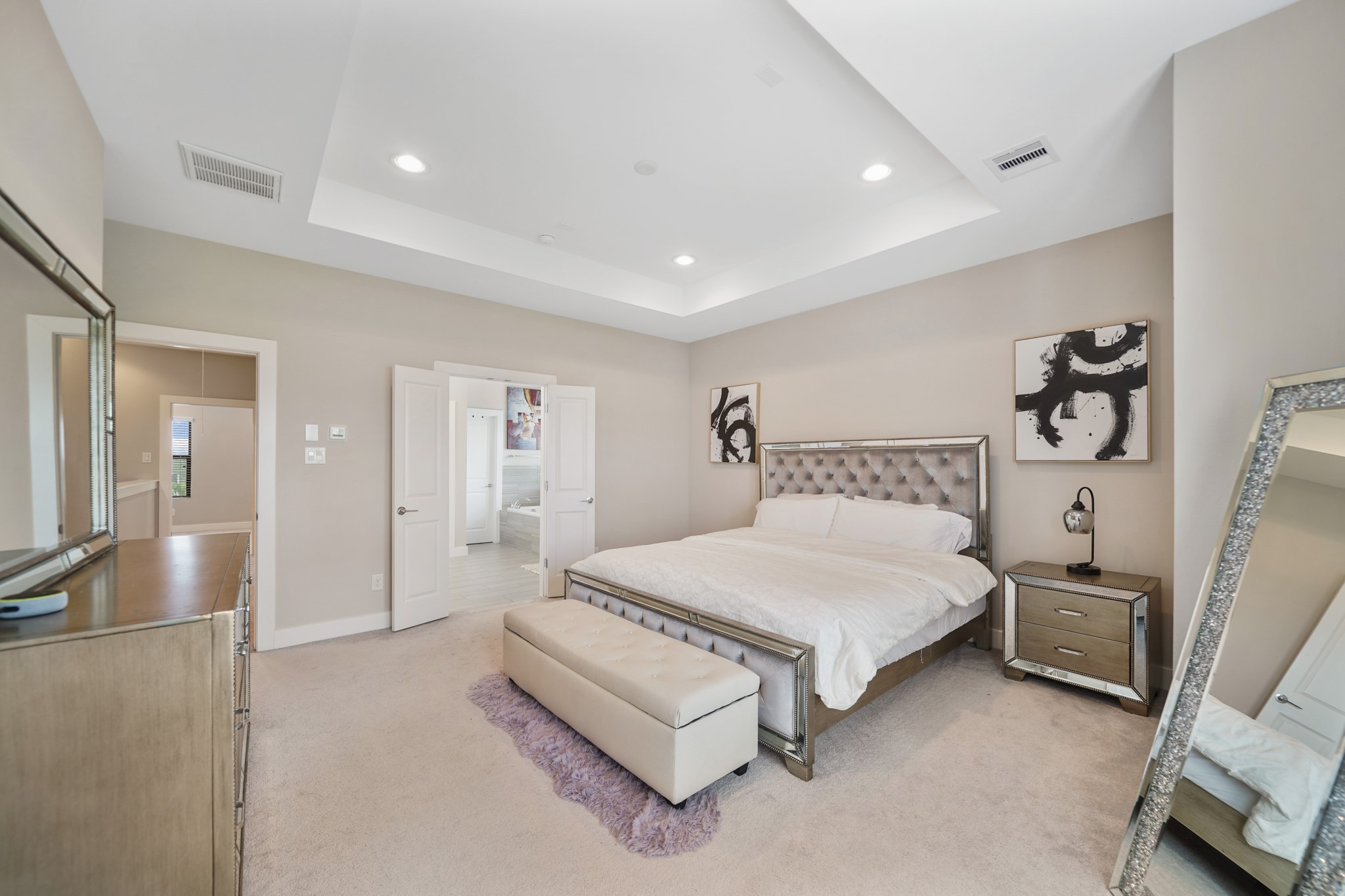 A view of the primary bedroom with the third floor corridor and access to a private bath shown in the background. The king size bed including frame & foam mattress can stay with the home along with the electronic mirror.