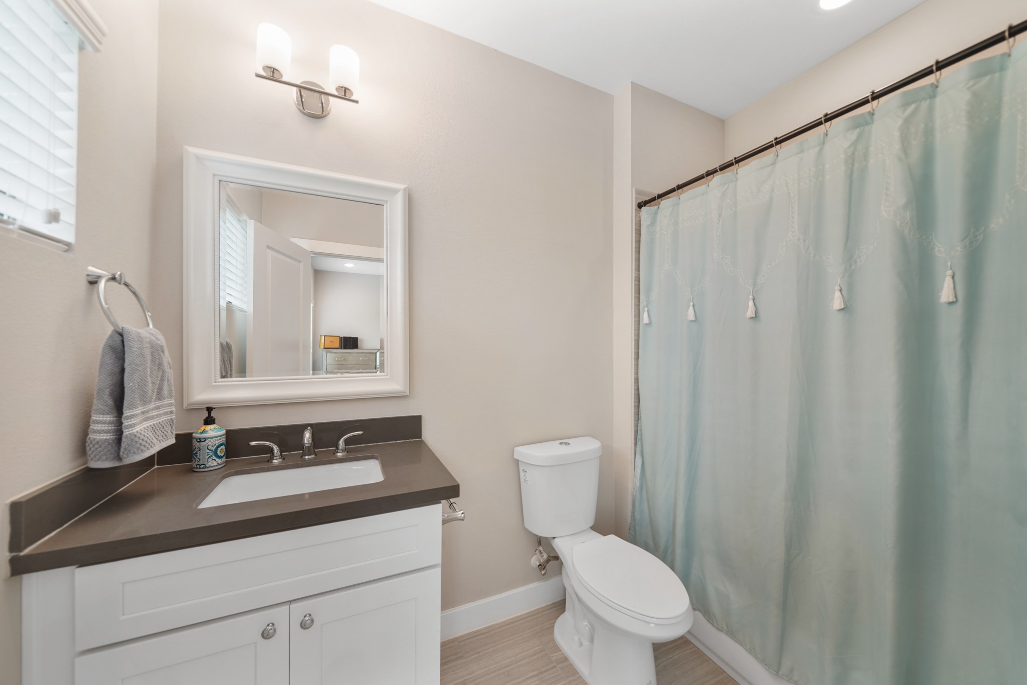 This private bath has a painted Shaker-style cabinet with a quartz counter top & integrated back splash highlighted by a framed mirror with wall mounted lighting above, a ceramic tile
surrounded combination tub/shower, window with blinds & tile floors.