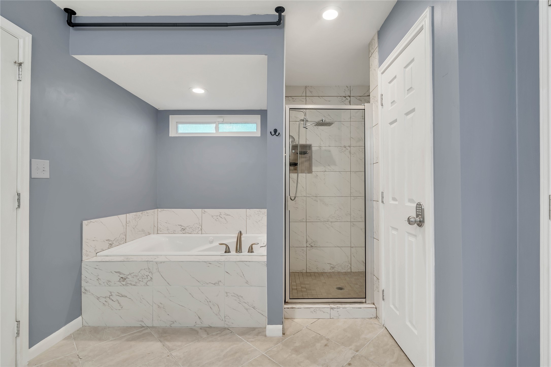 Relax in the spacious primary bath, featuring a deep soaking tub with marble-look tile surround, a separate tiled walk-in shower with rainfall showerhead, and a clean, contemporary design.