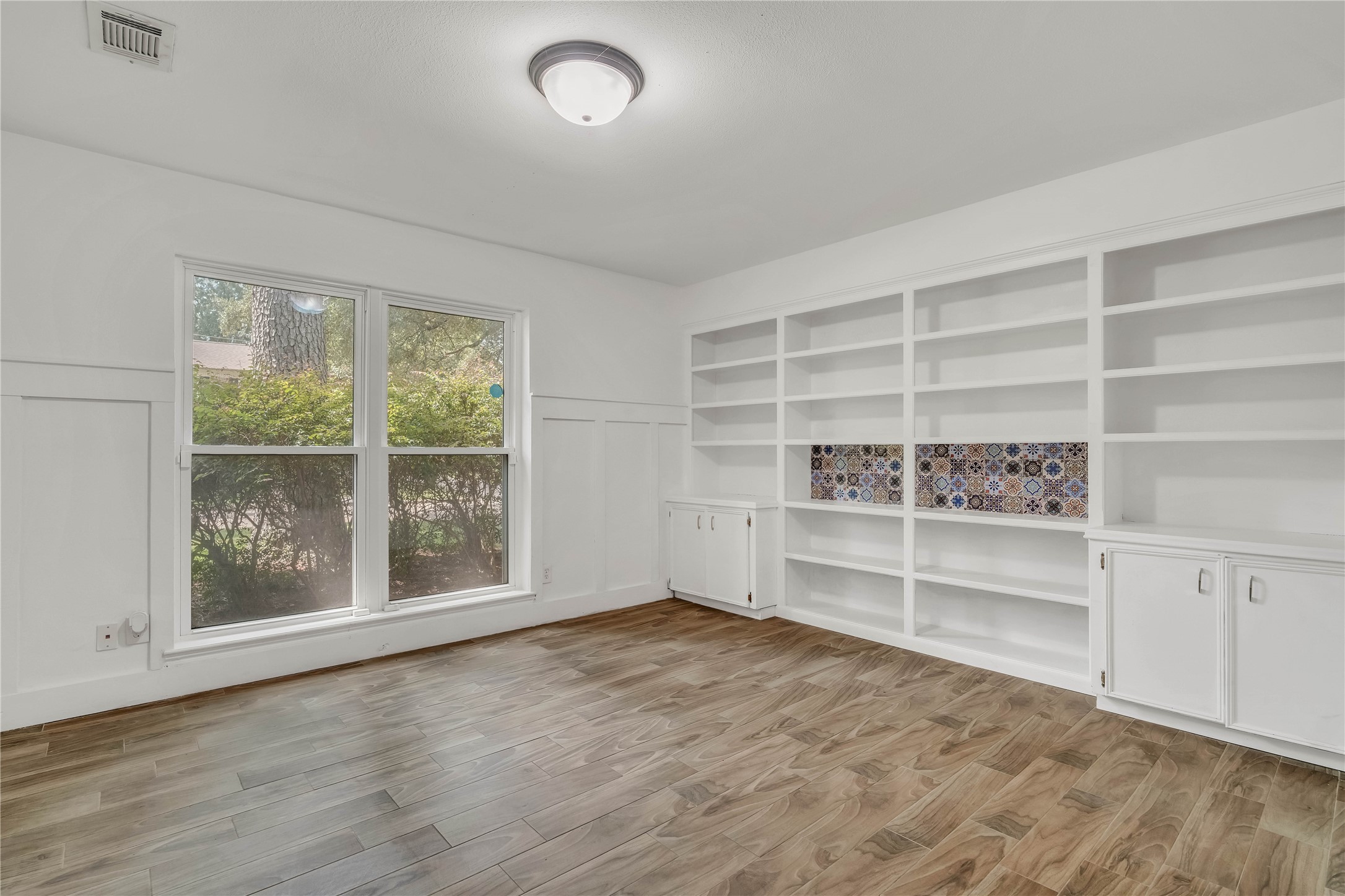 Expansive downstairs home office featuring an impressive wall of built-in shelving and cabinetry, abundant natural light, and exceptional space for a sophisticated home office.