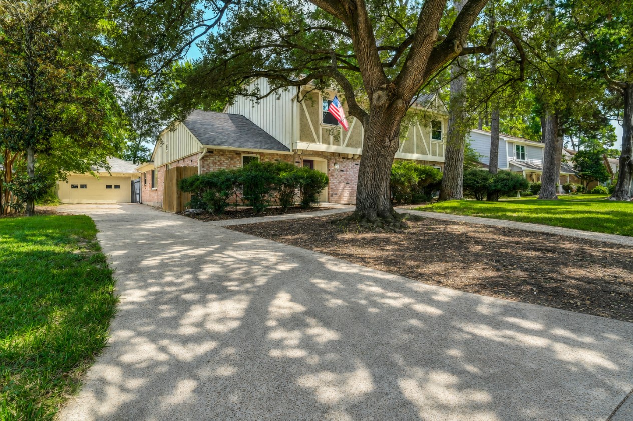 Side exterior view highlighting the extended driveway leading to the detached garage, surrounded by mature trees and established landscaping. Side exterior view highlighting the extended driveway leading to the detached garage, surrounded by mature trees and established landscaping.