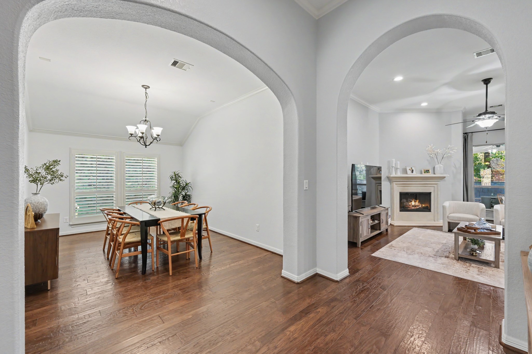 Elegant open-concept living and dining area featuring beautiful hardwood floors, graceful archways, and a cozy fireplace, perfect for entertaining and relaxation.