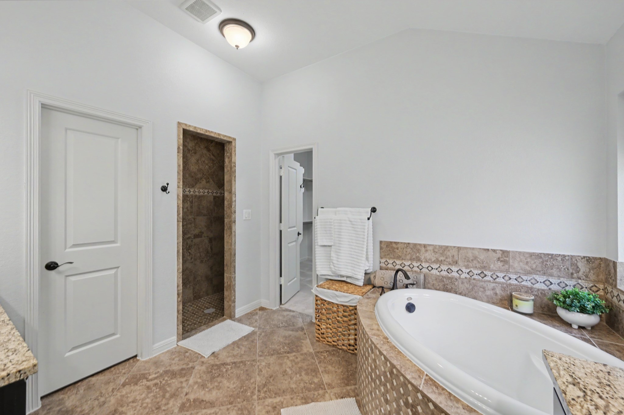 Luxurious bathroom featuring a spacious corner bathtub with elegant tile accents, a walk-in shower, and ample natural light for a serene atmosphere.